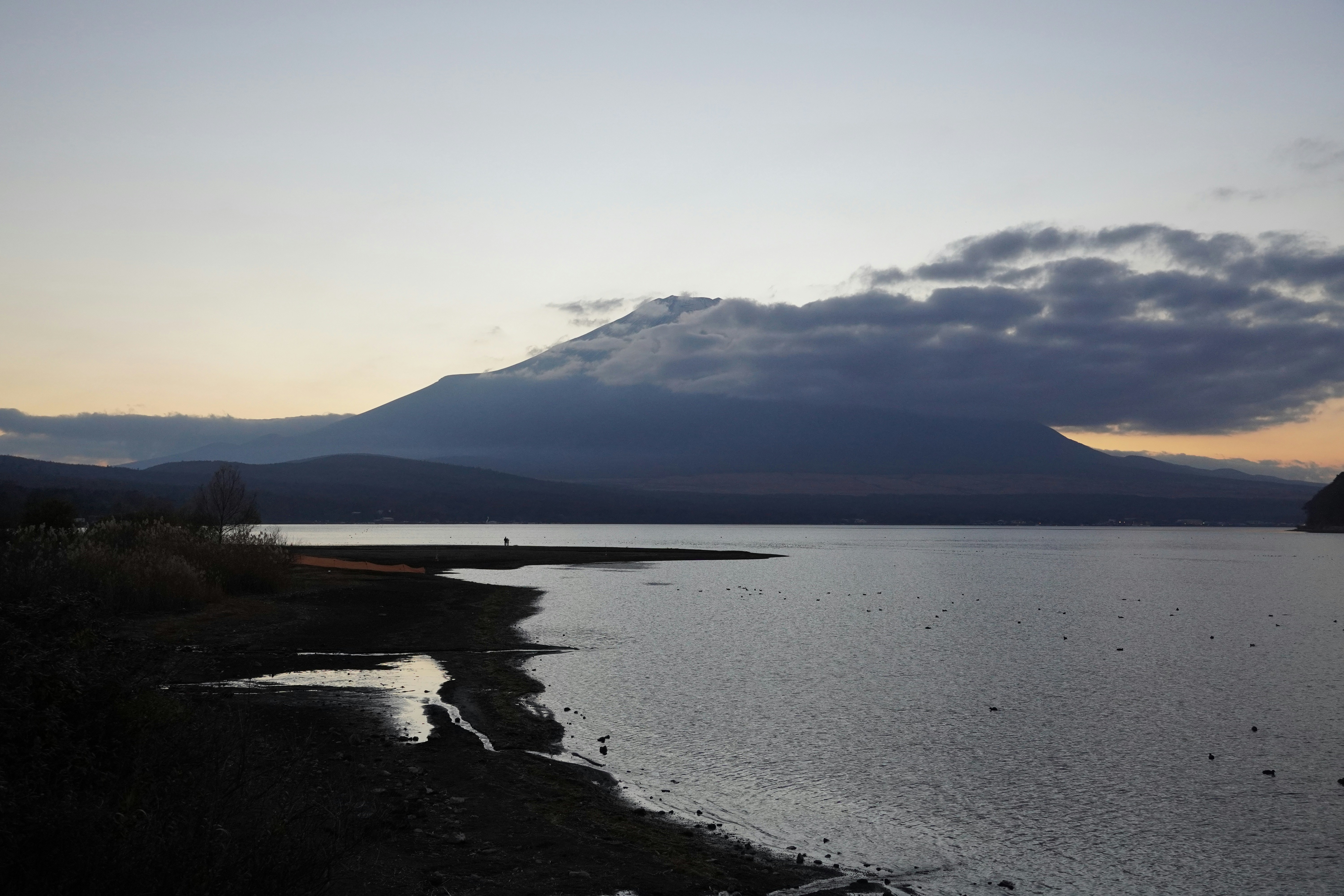 Mountain peak shrouded in clouds over a calm lake.