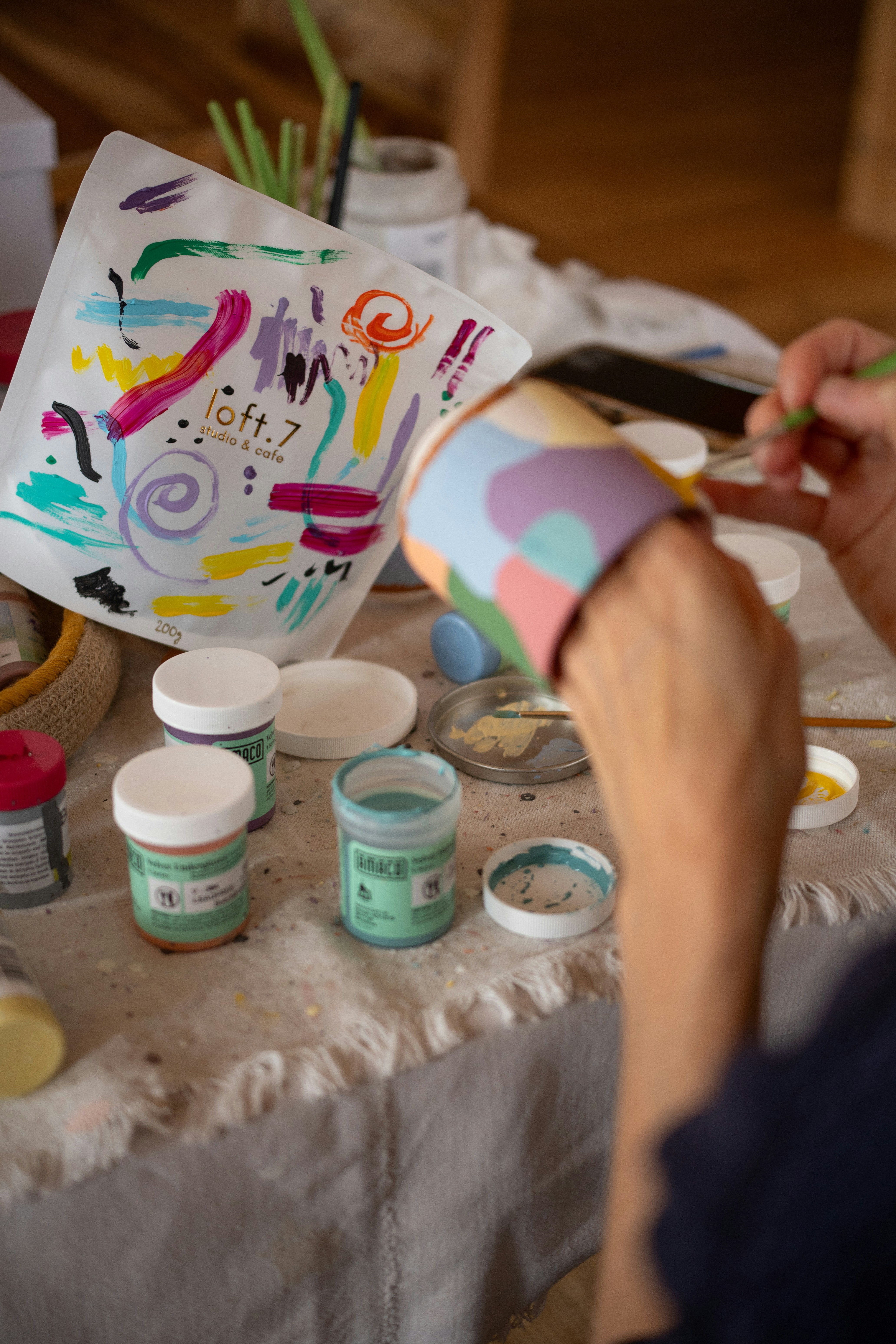 Hands painting a colorful abstract design on a cup.