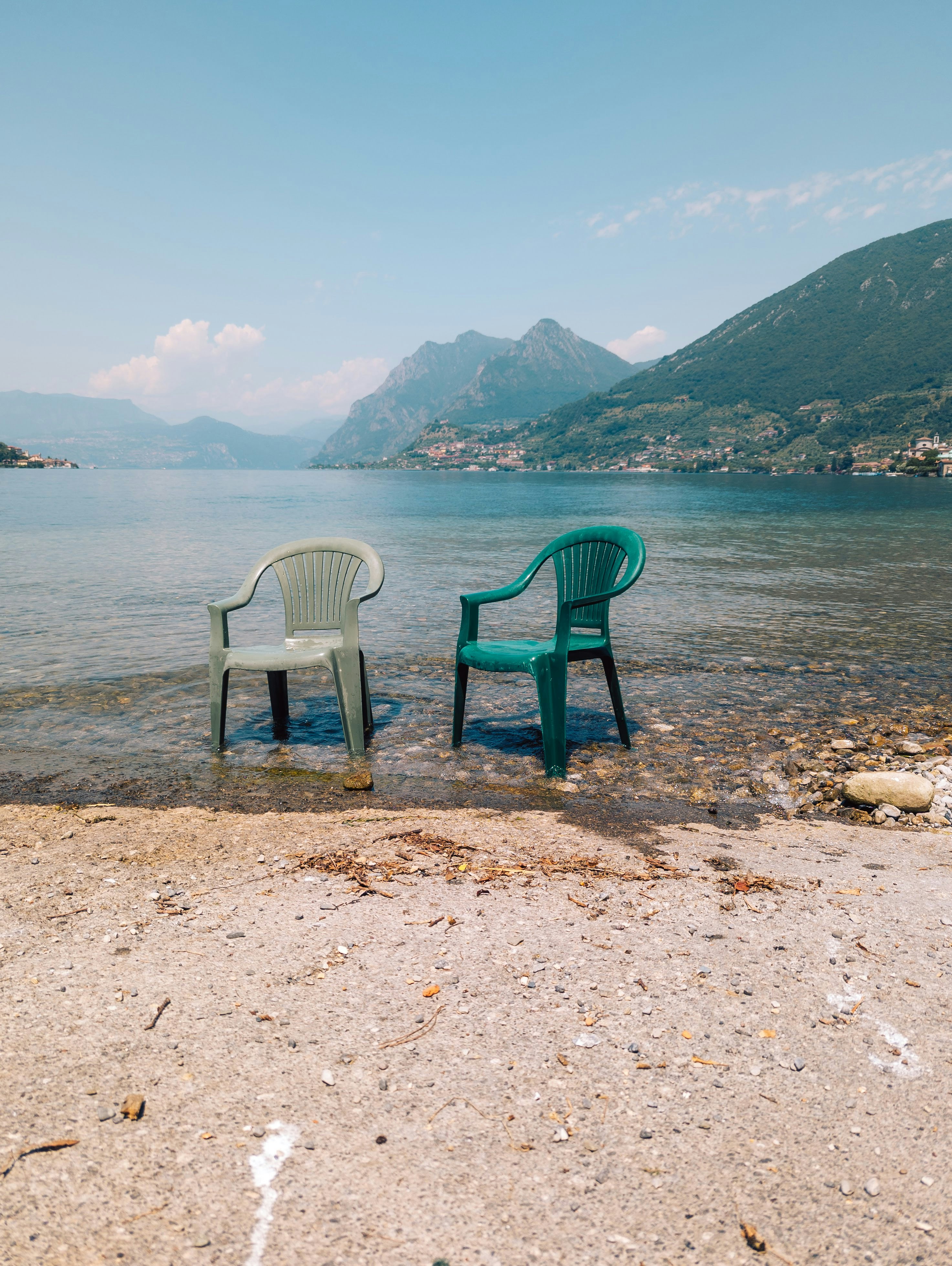 Two plastic chairs on a beach overlooking a lake.
