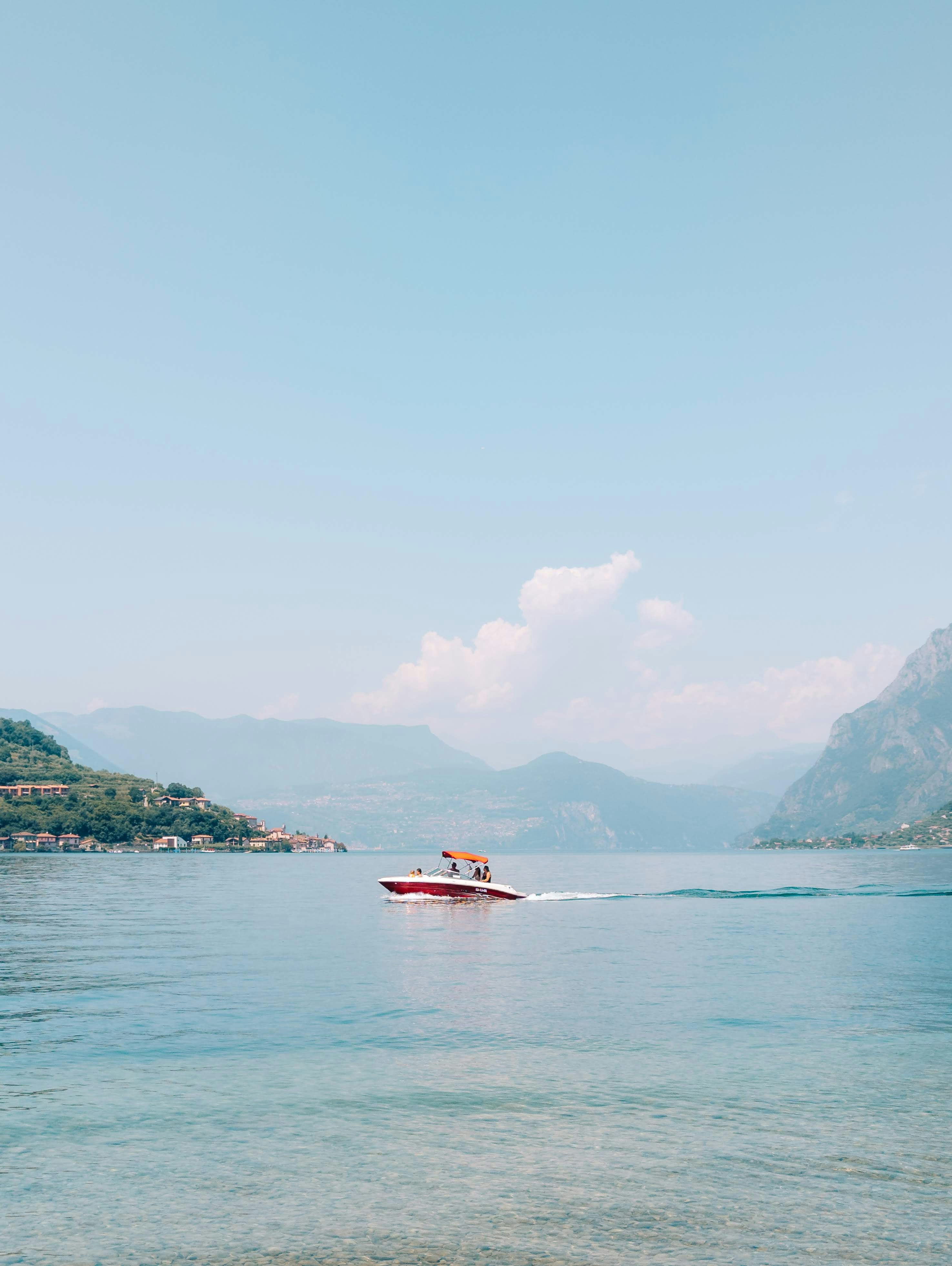 Red boat sailing on a calm blue lake with mountains.