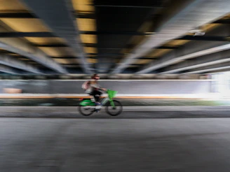 Person riding a green bicycle under a bridge