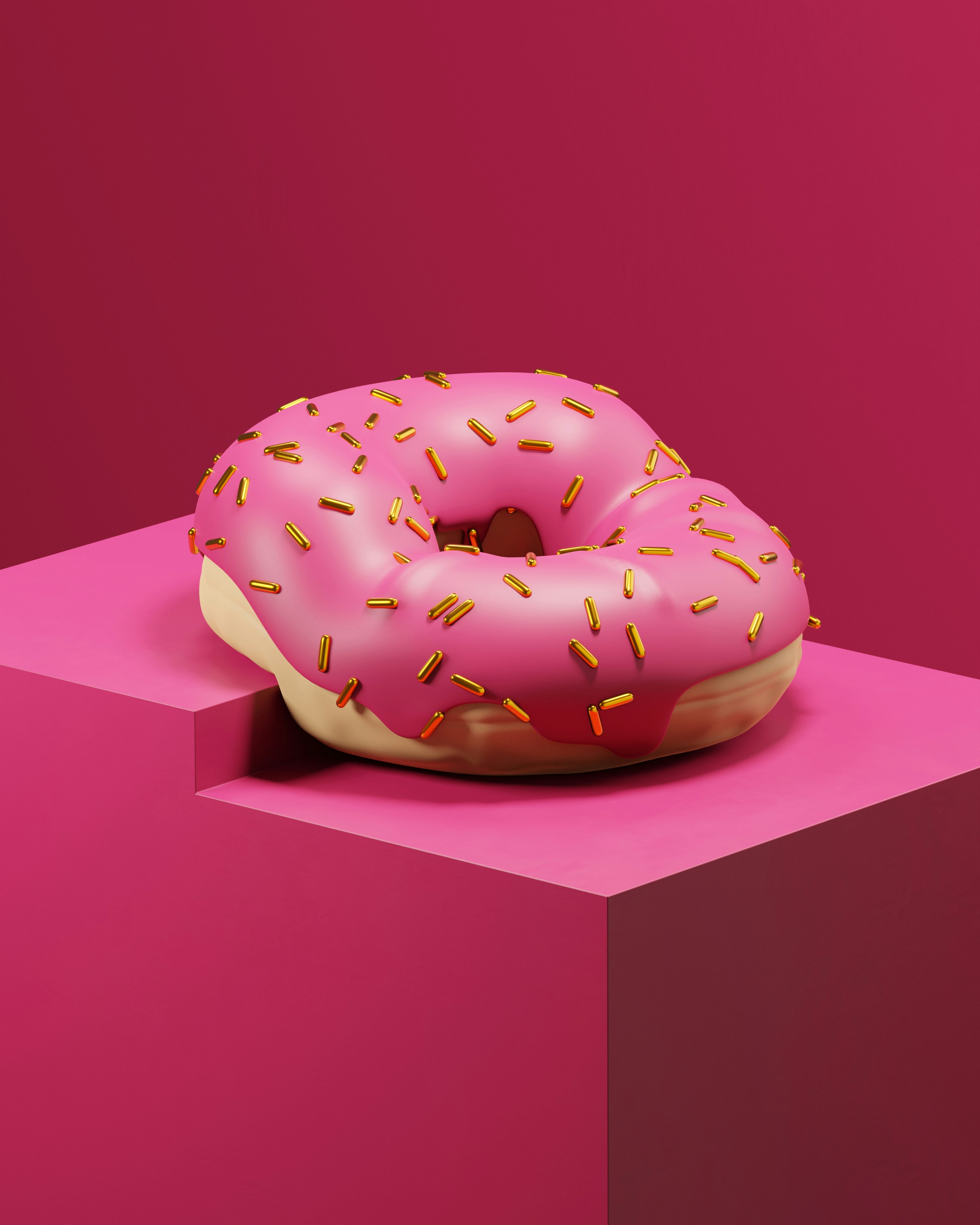Pink frosted donut with gold sprinkles on a pink cube
