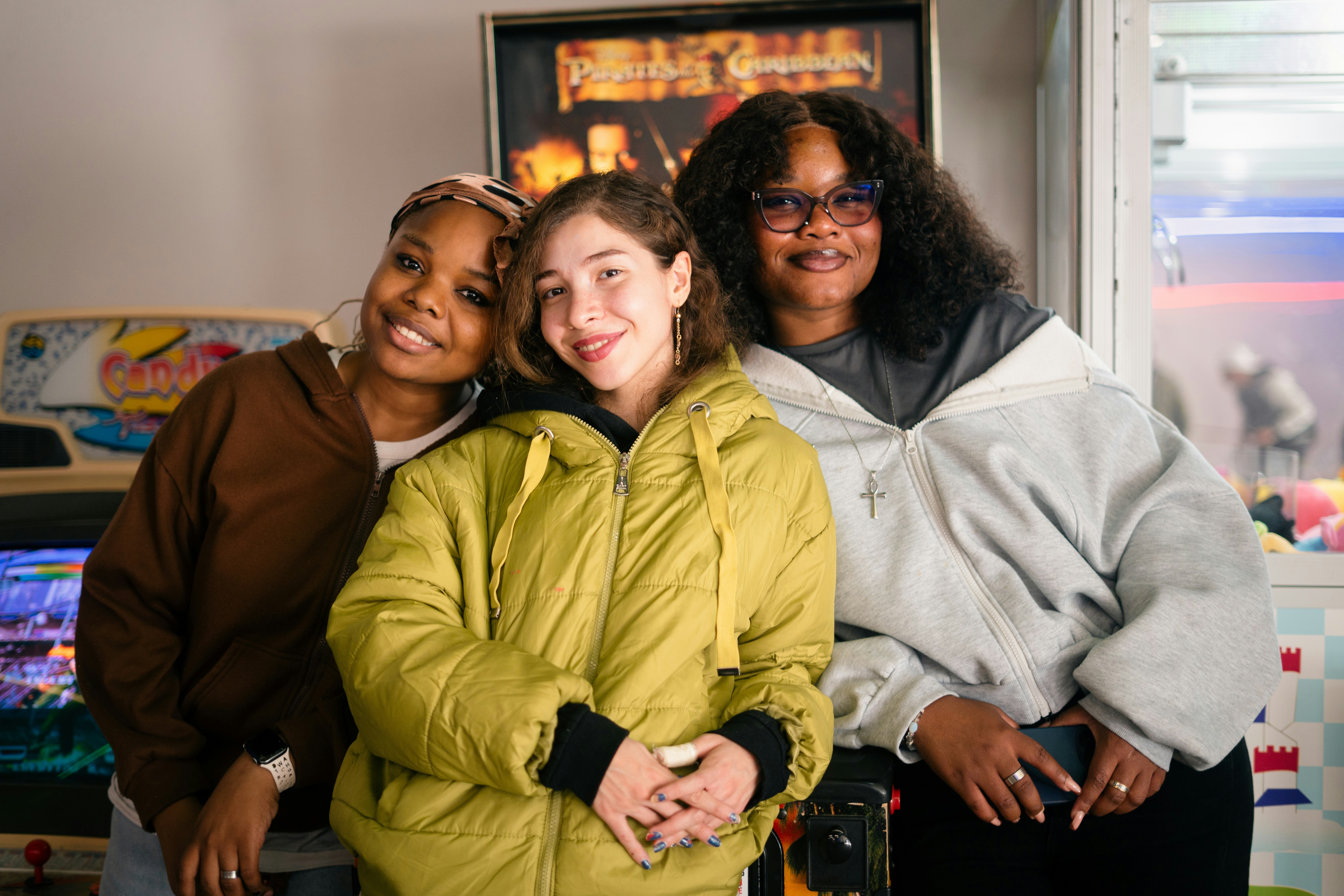 Trois amis posant ensemble devant des jeux d’arcade.