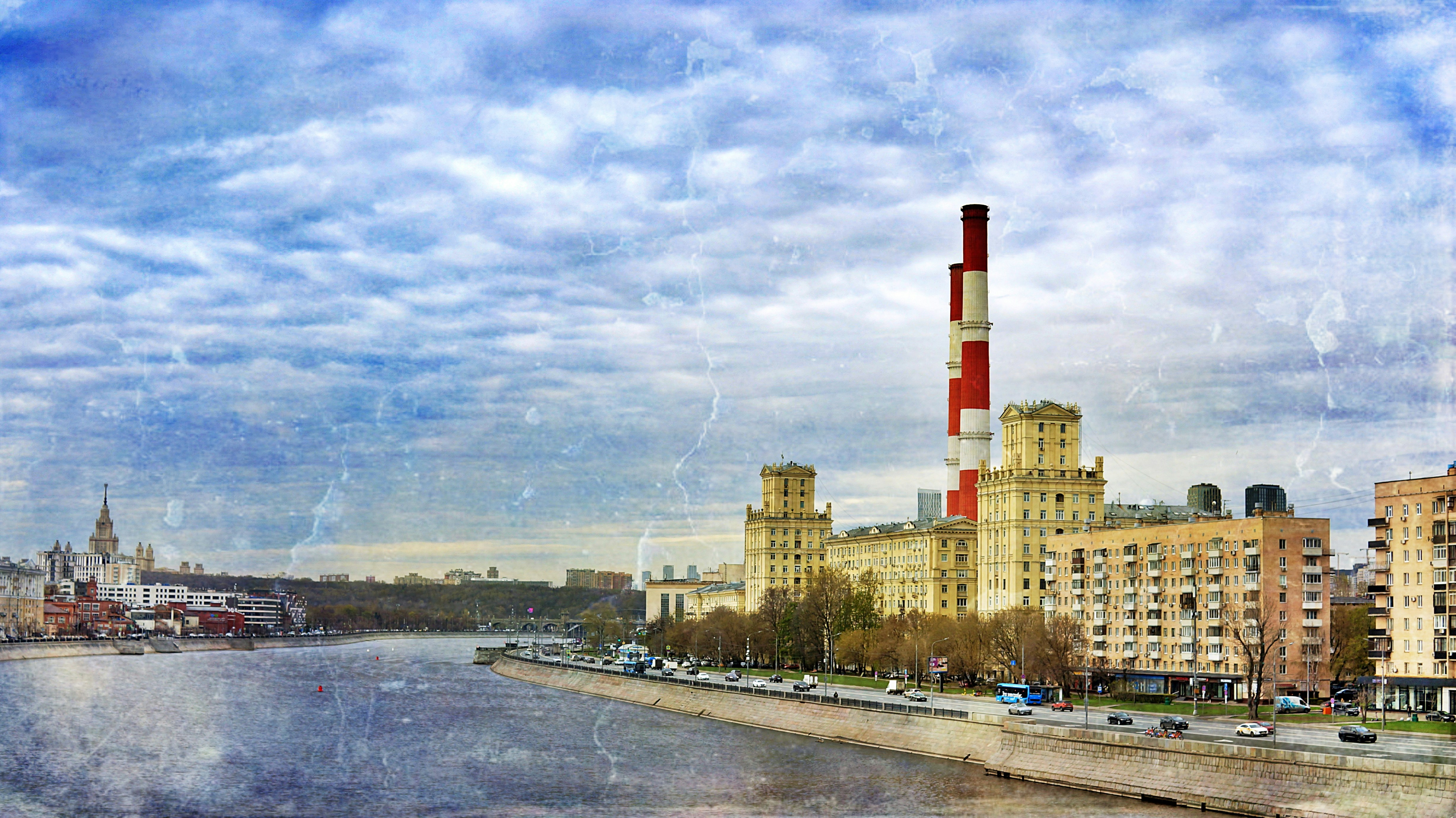 Cityscape with river and industrial smokestacks.