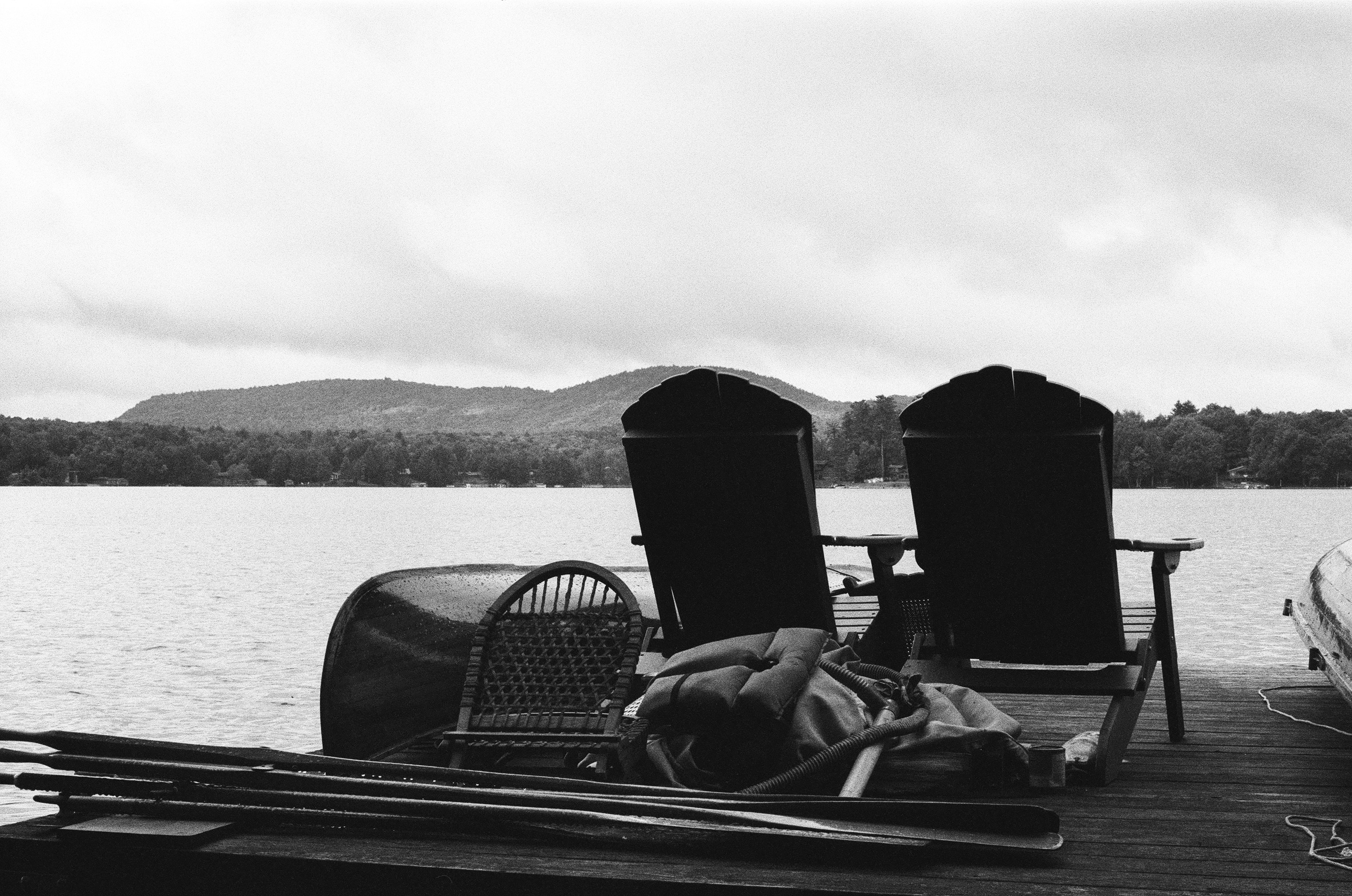 Two adirondack chairs on a dock by a lake