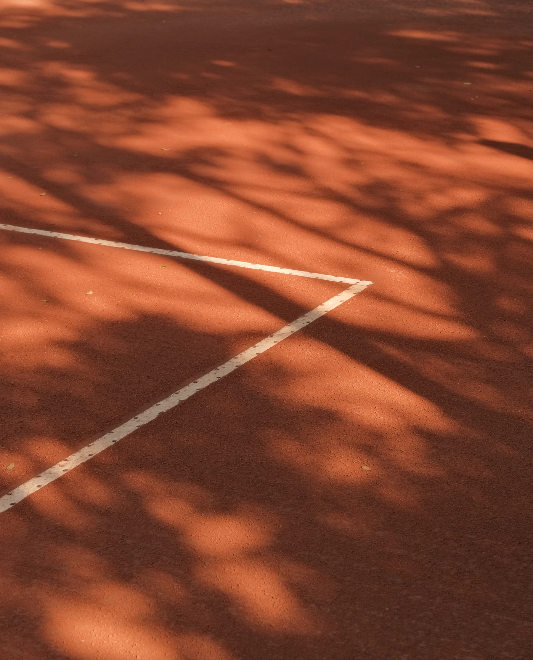 Tree shadows falling across a red clay court and its white line