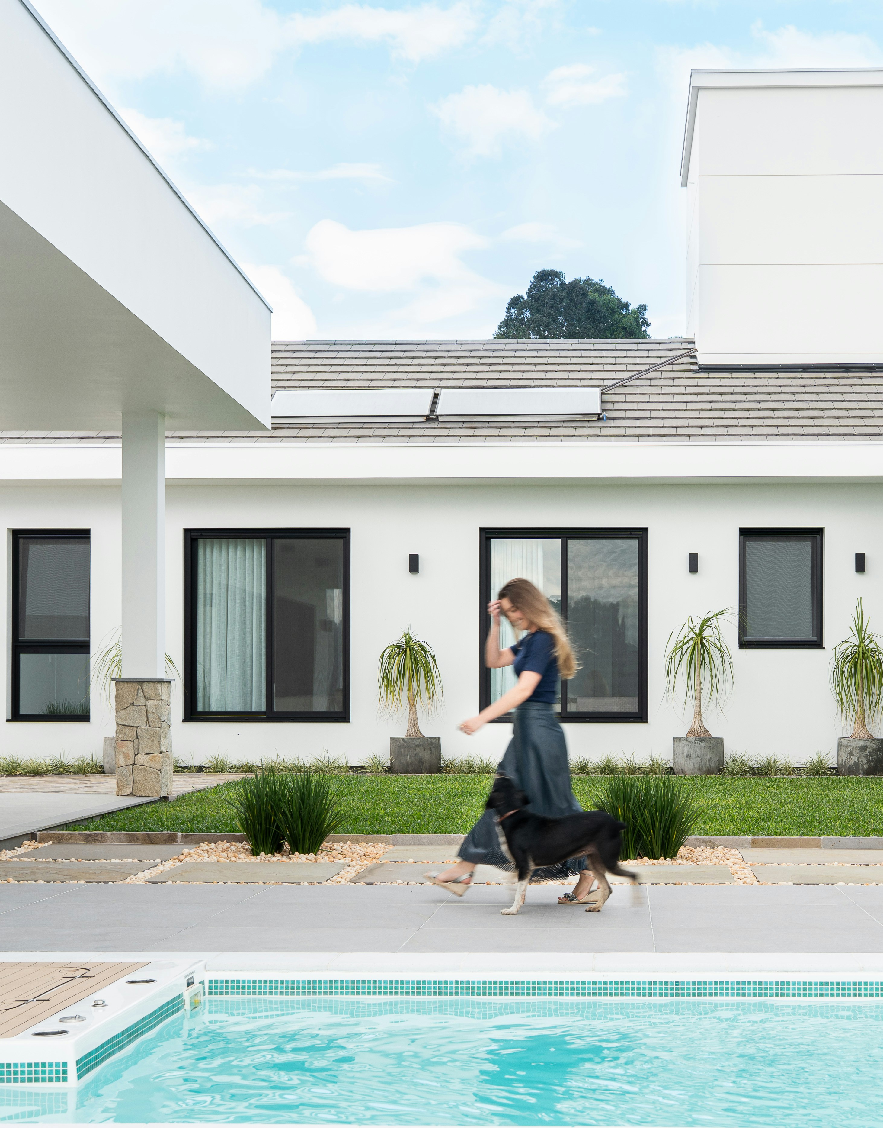 Frau, die mit einem Hund in der Nähe eines modernen Hauses und Pools spazieren geht