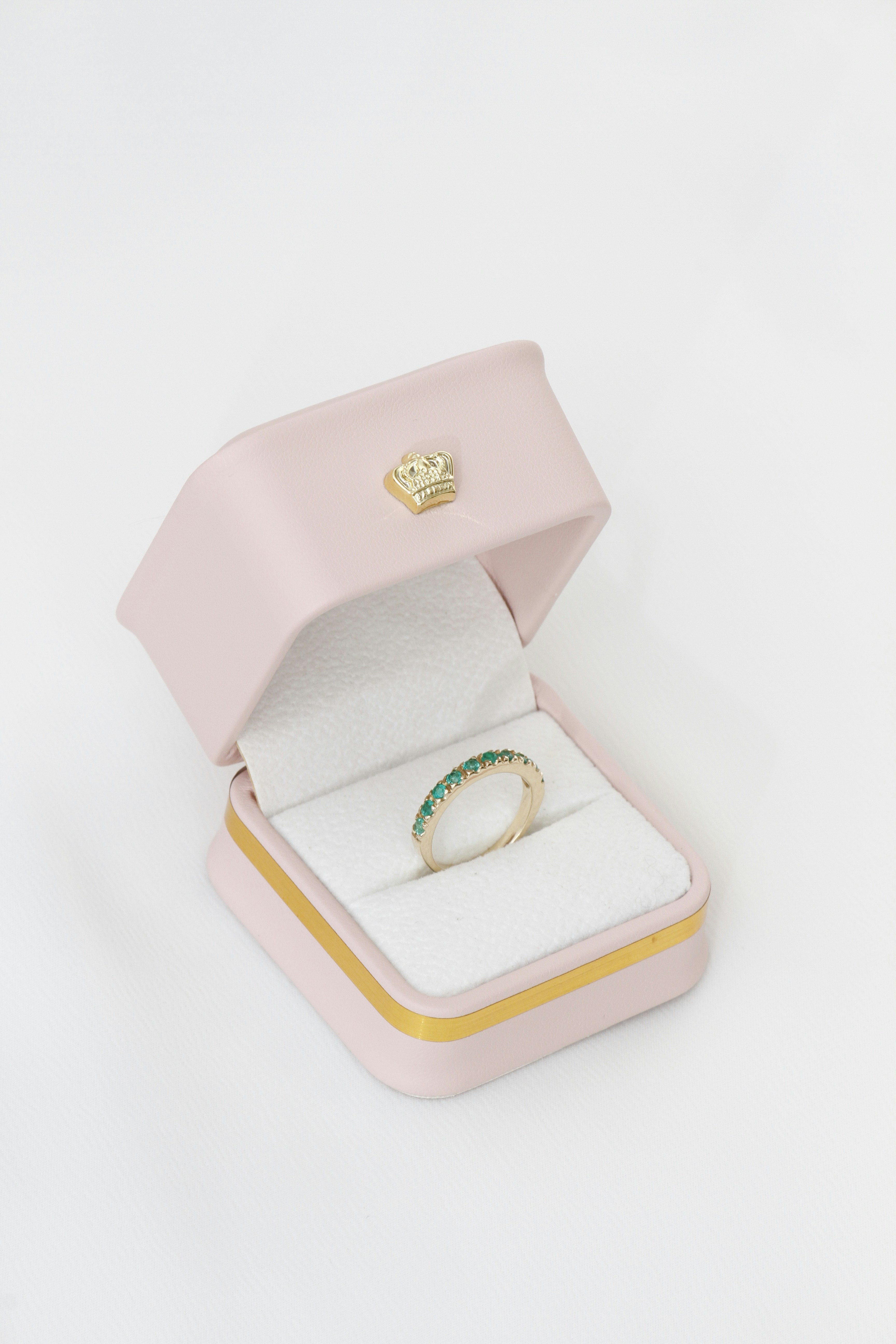 Goldring mit grünen Edelsteinen in einer rosa Schachtel