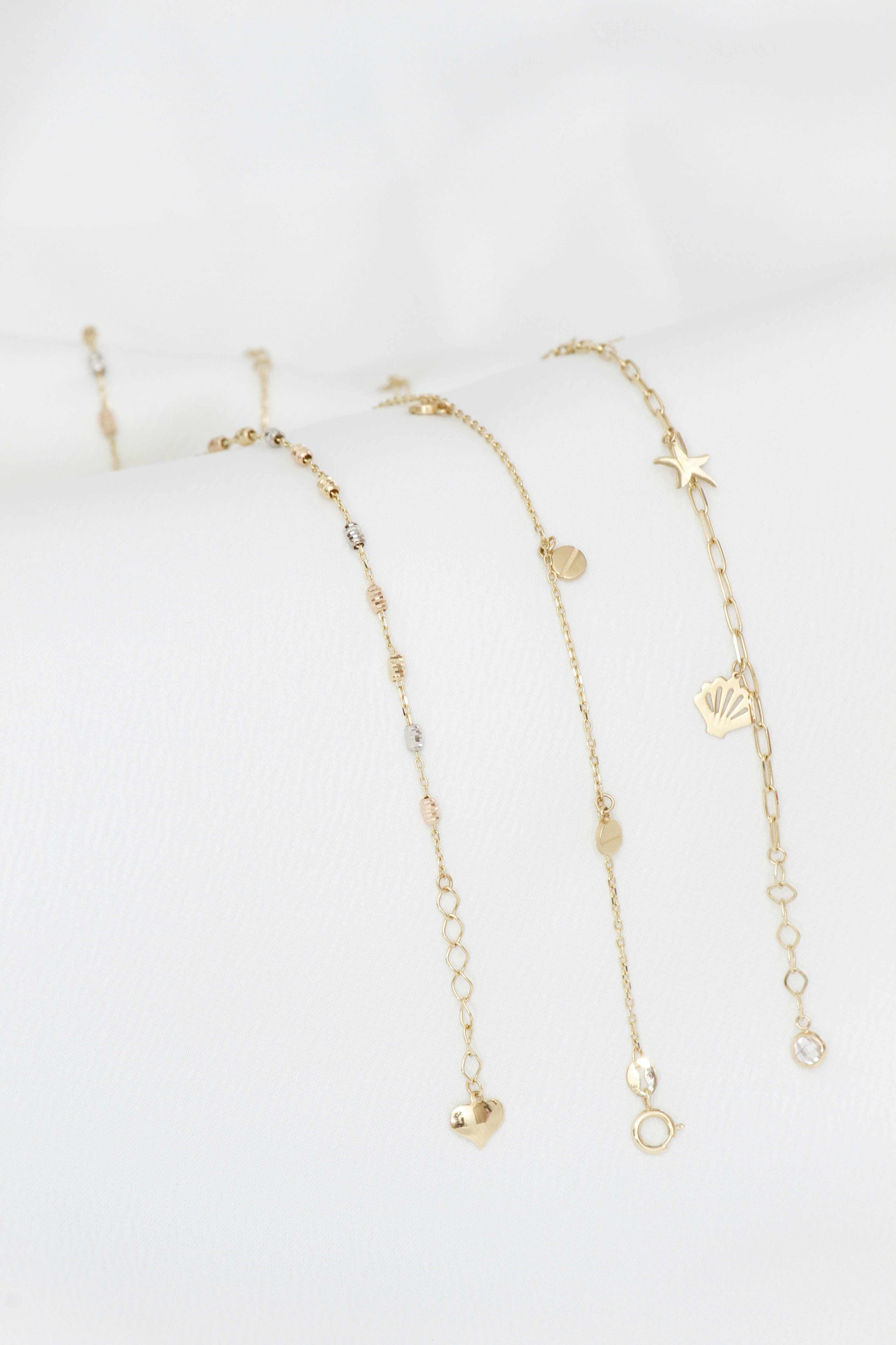 Zarten goldene Armbänder mit Anhängern auf weißem Hintergrund