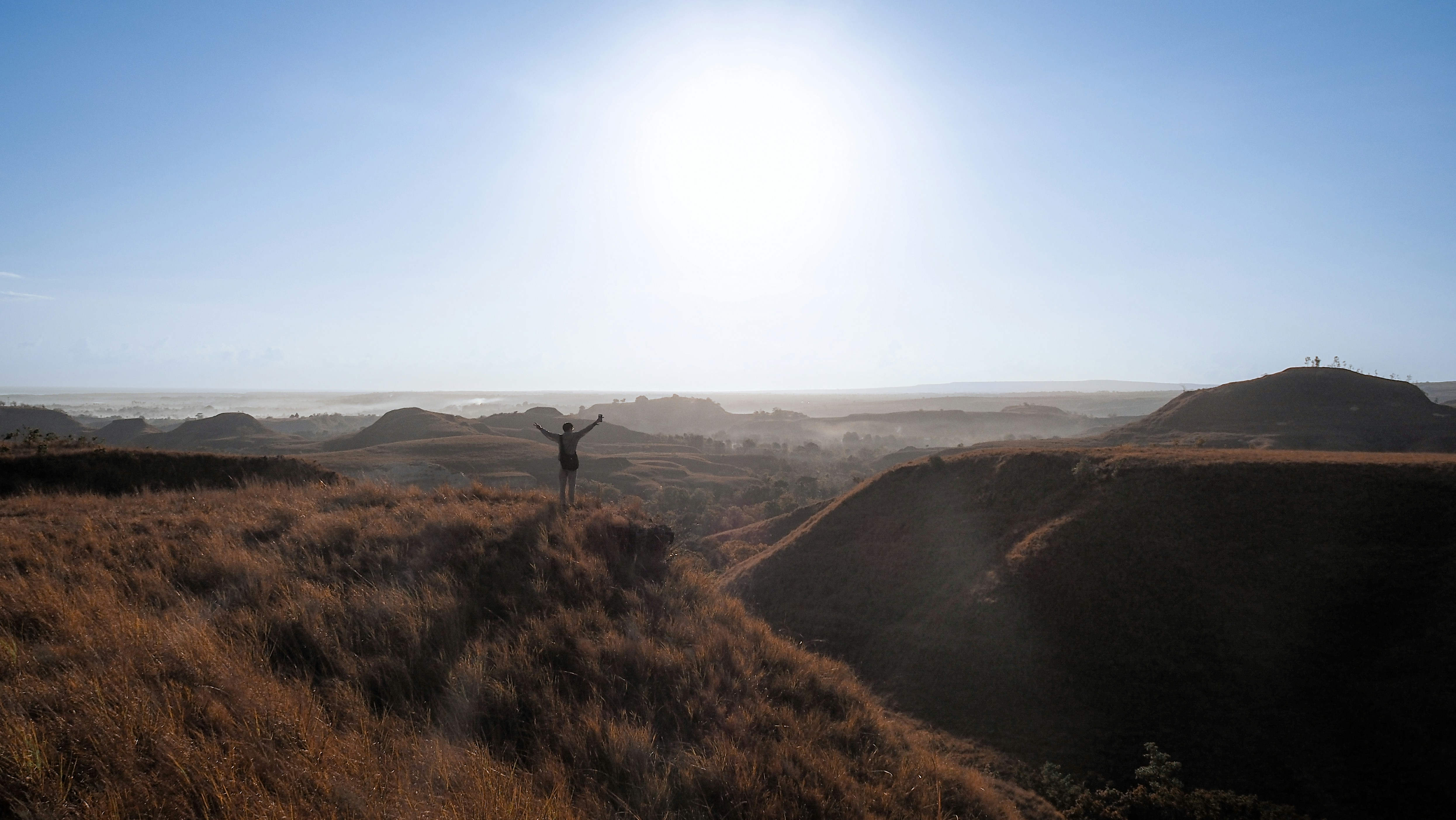 Person with arms raised on grassy hilltop at sunrise