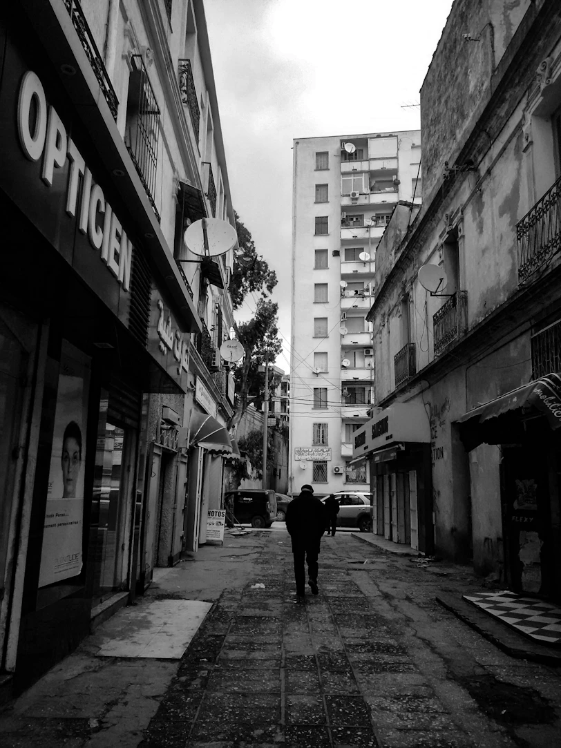 A lone figure walks down a narrow urban street.