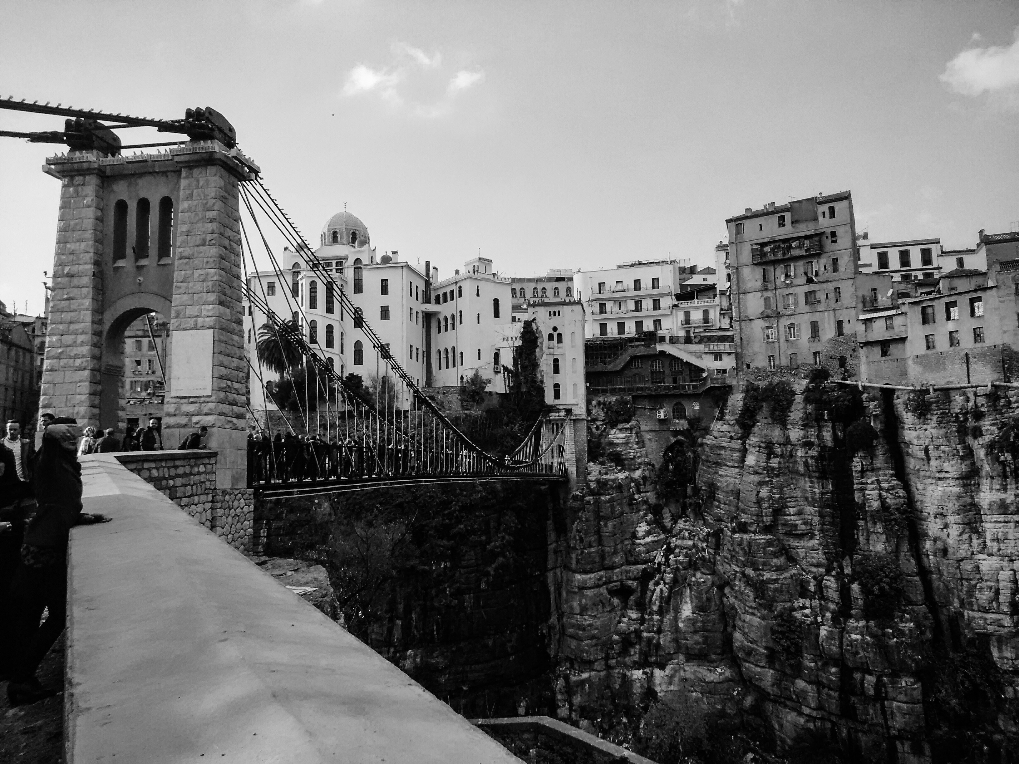 Suspension bridge over a rocky gorge with buildings.