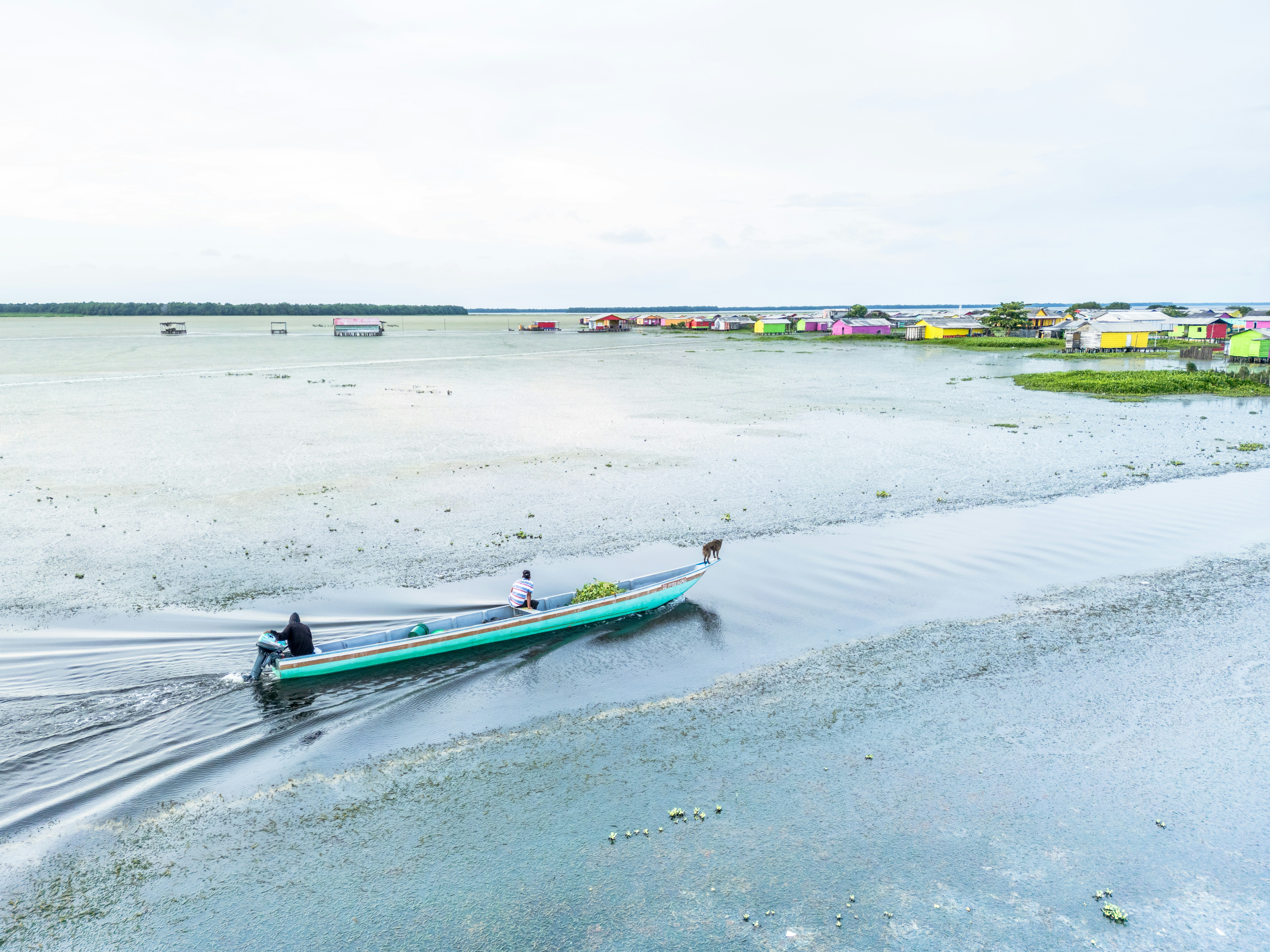 Man in a boat navigates shallow water near colorful village.