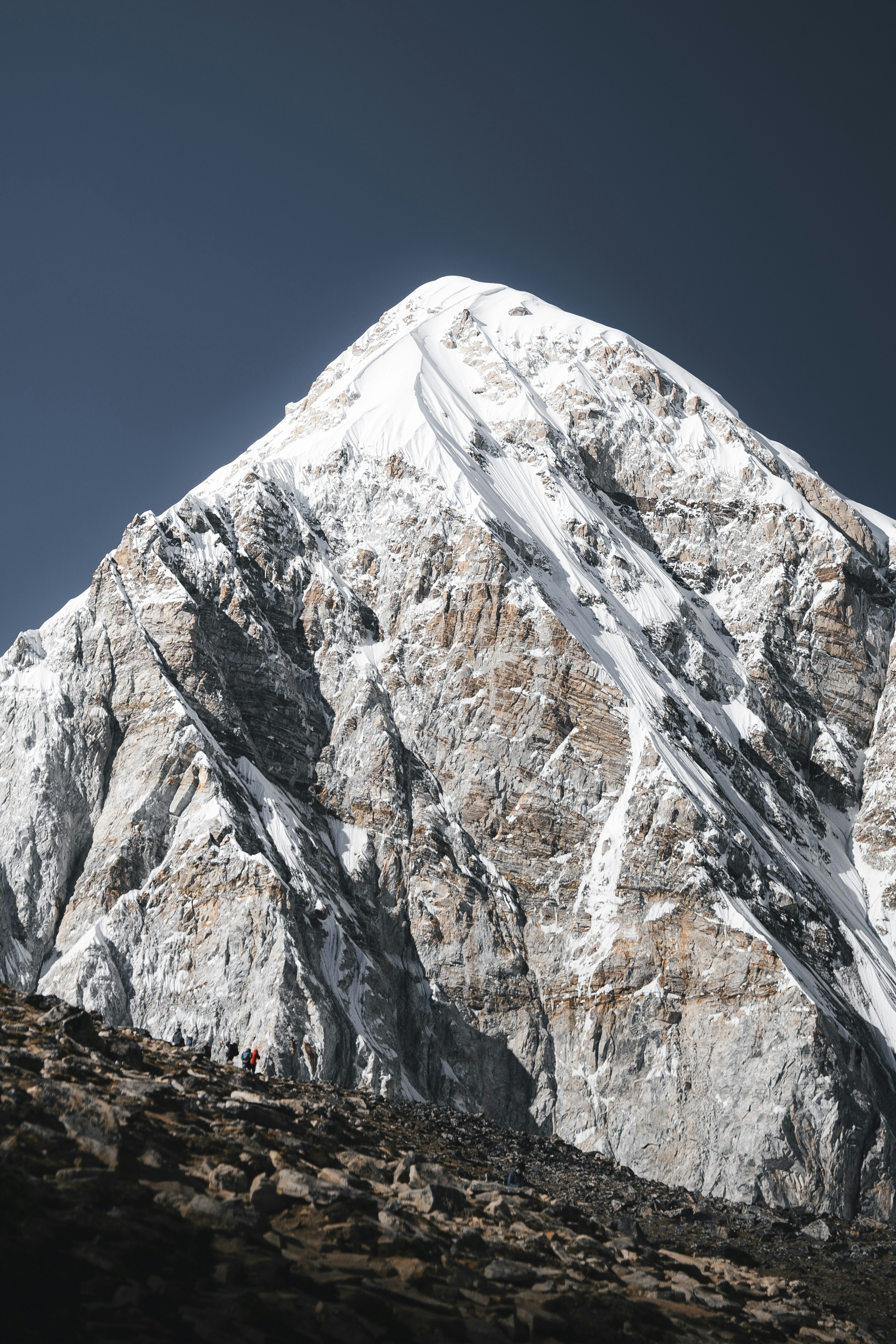 Cima montuosa coperta di neve con escursionisti su pendii rocciosi.