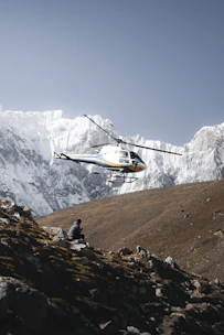 A helicopter flies over a person sitting on a mountain.