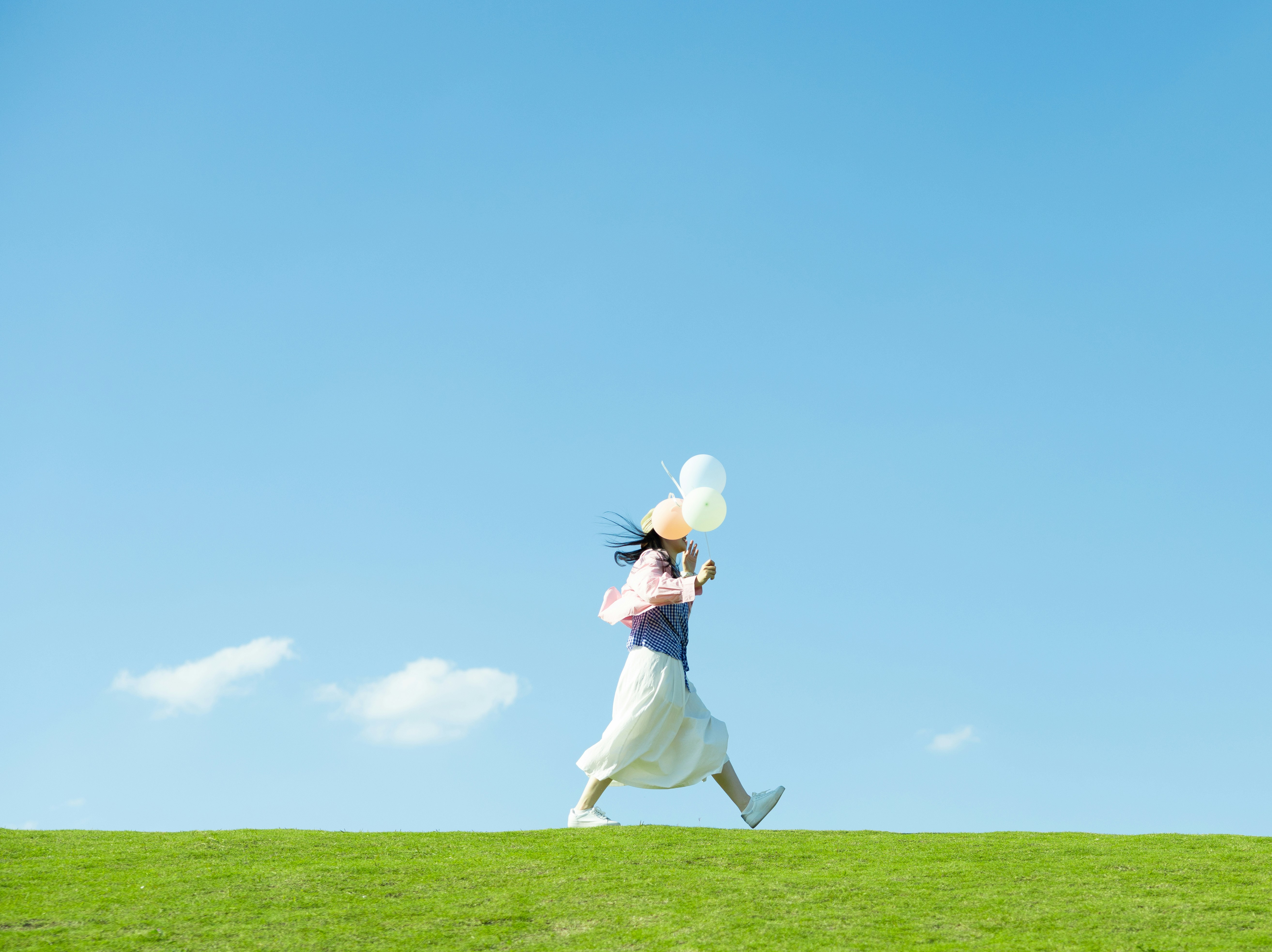 Frau, die mit Luftballons auf einem grasbewachsenen Hügel läuft