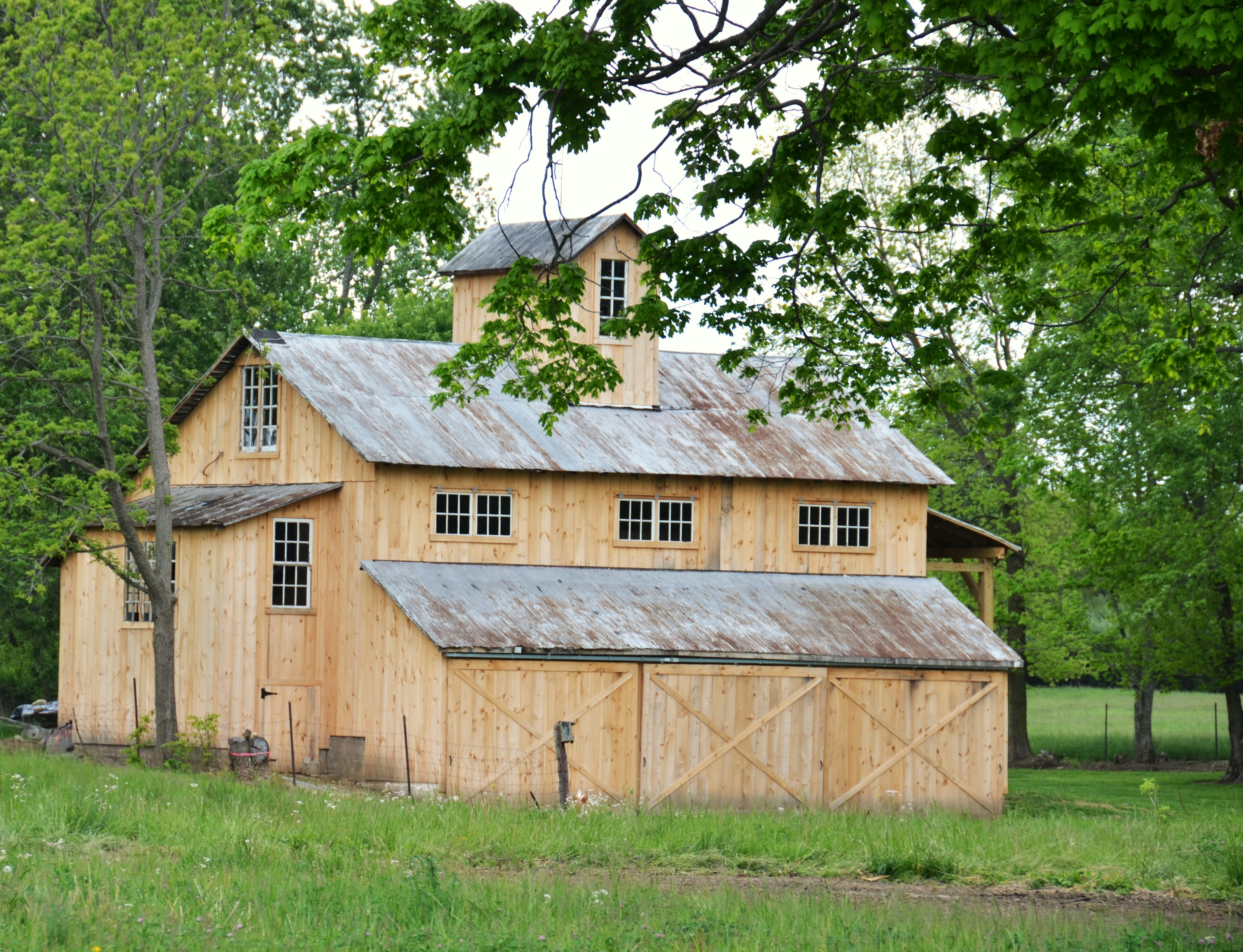 Une grange en bois avec un toit métallique entourée d’arbres.