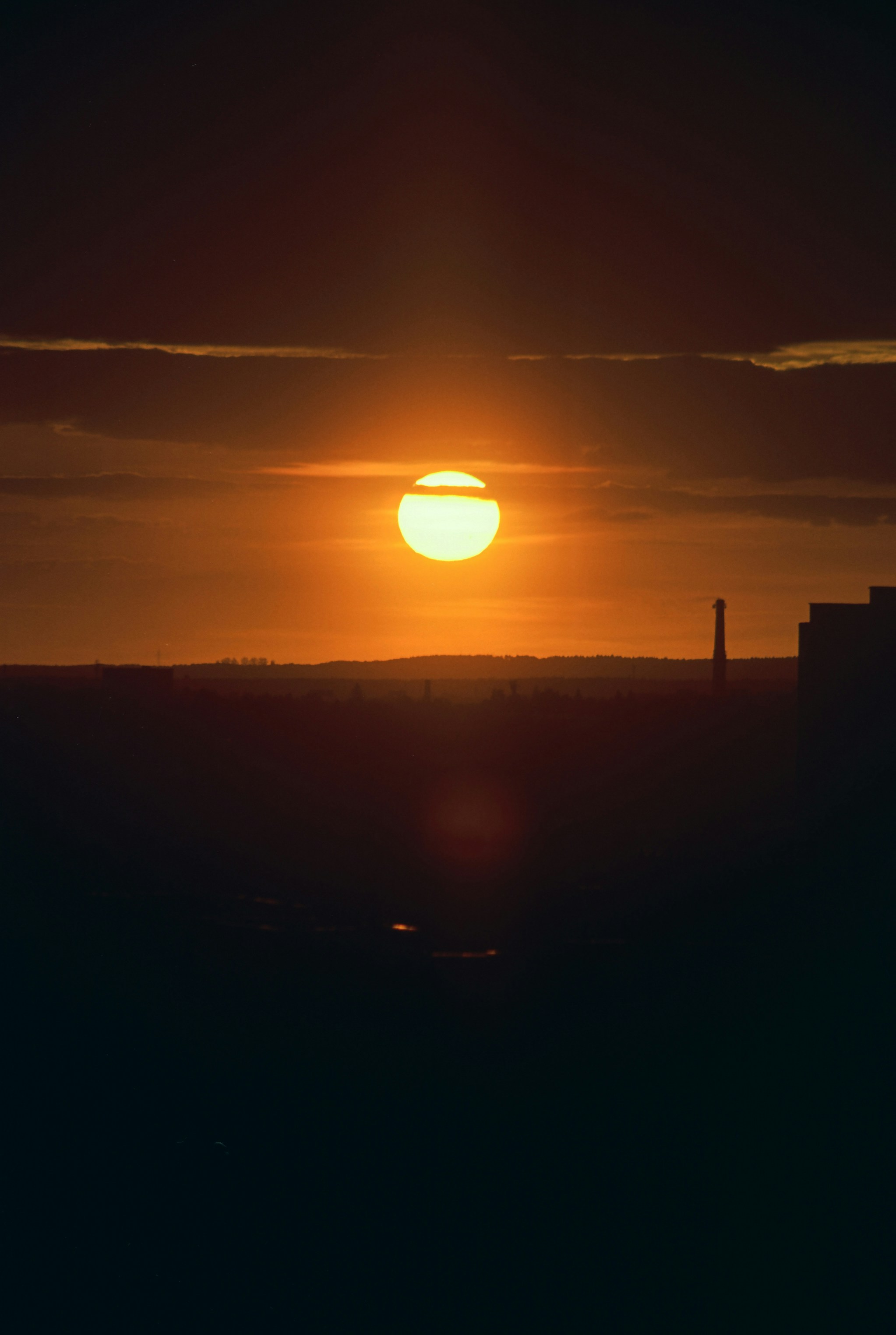 Golden sun setting over a dark cityscape silhouette