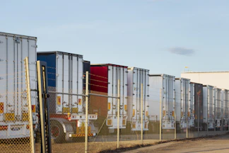 Row of parked semi-trailer trucks behind a fence