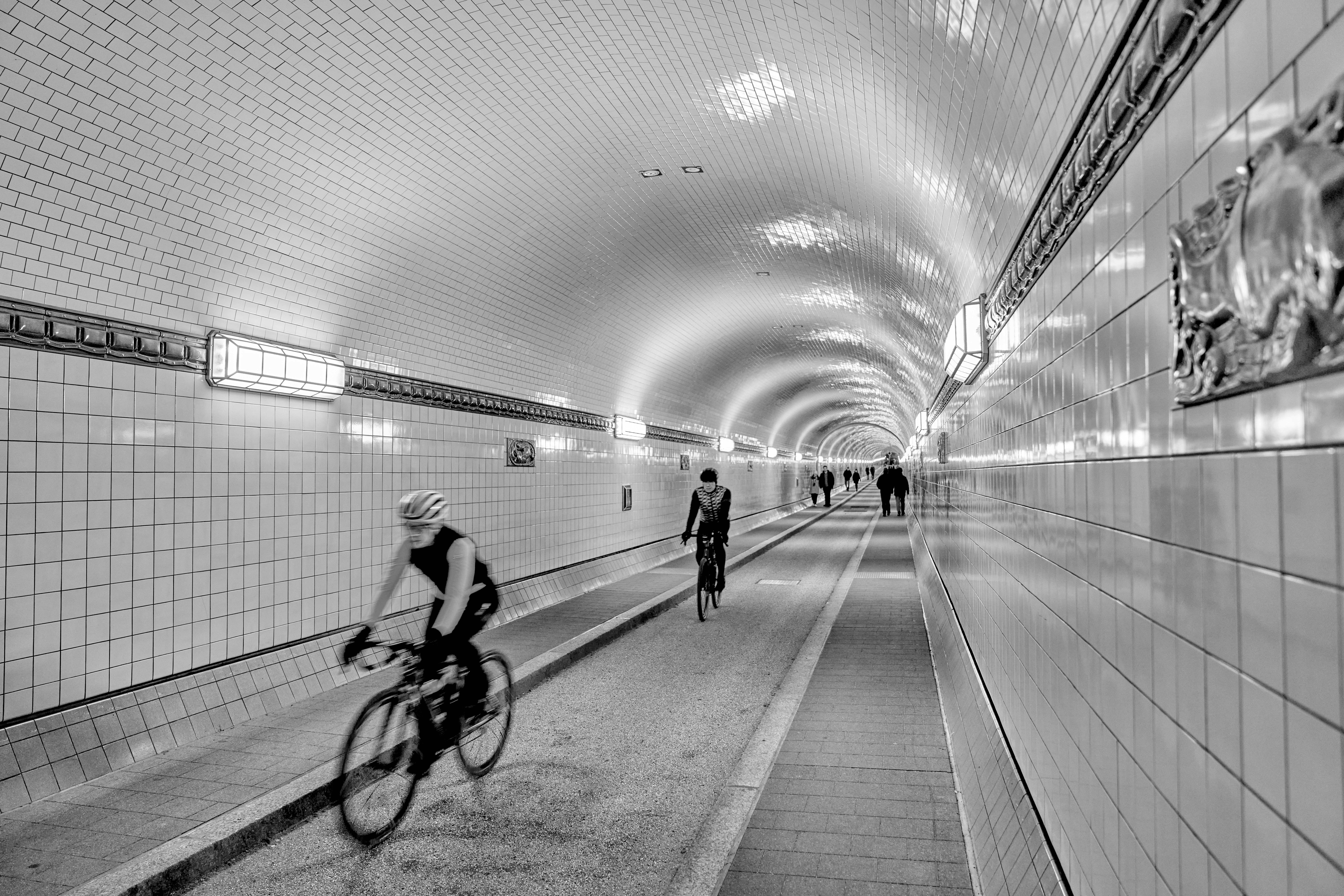 Cyclists riding through a tiled tunnel with lights