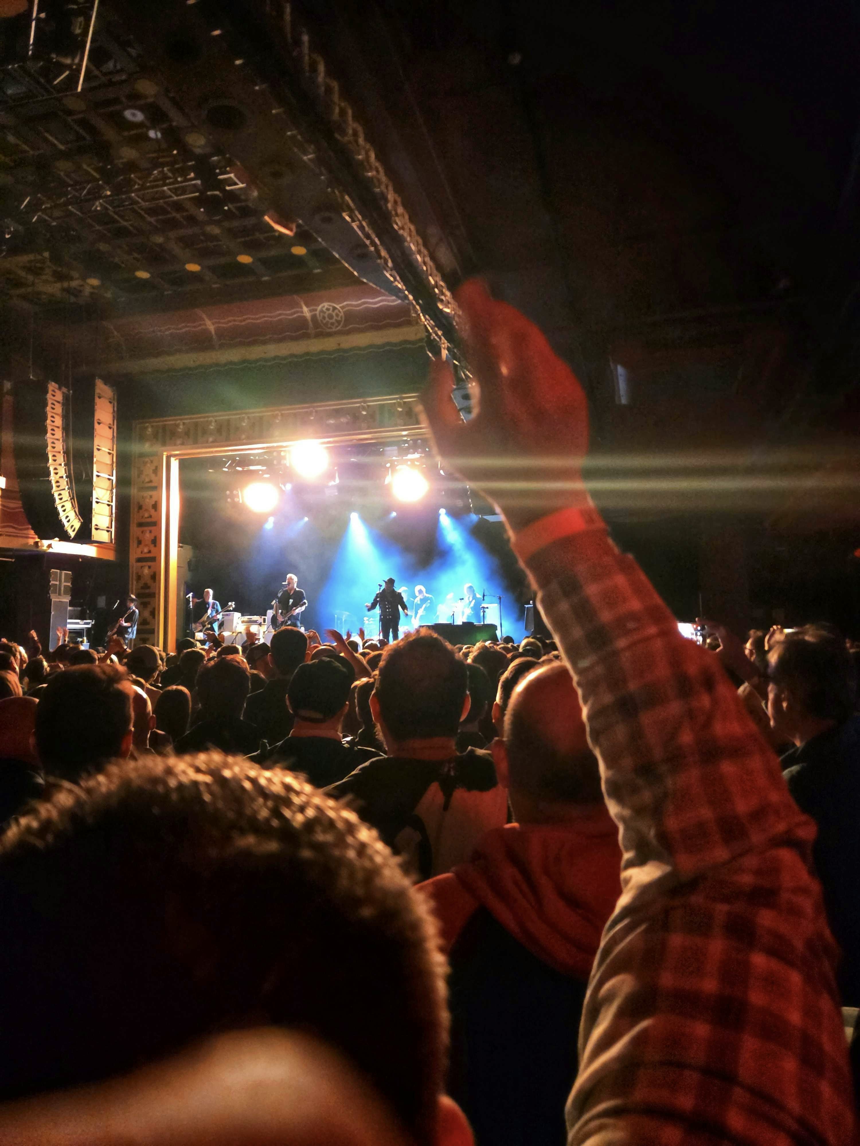 Il pubblico del concerto assiste alla band esibirsi su un palco illuminato a piena luce.