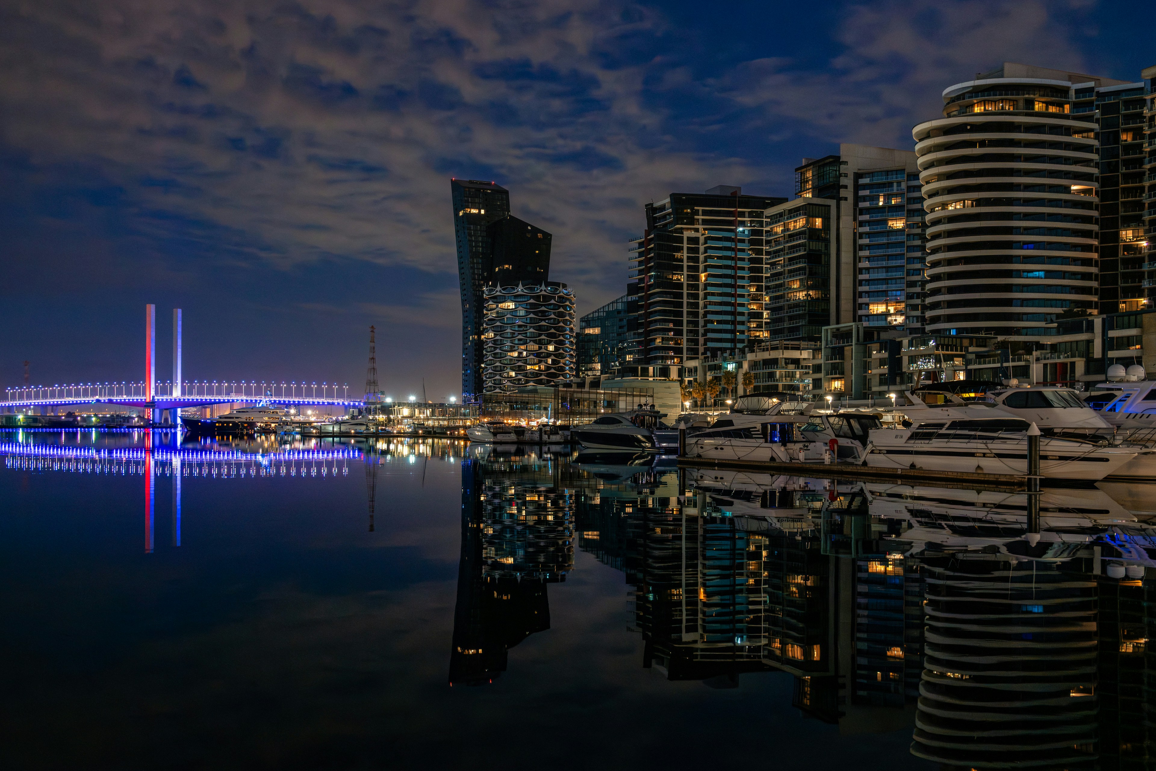 Cityscape with bridge and yachts reflected in water at night