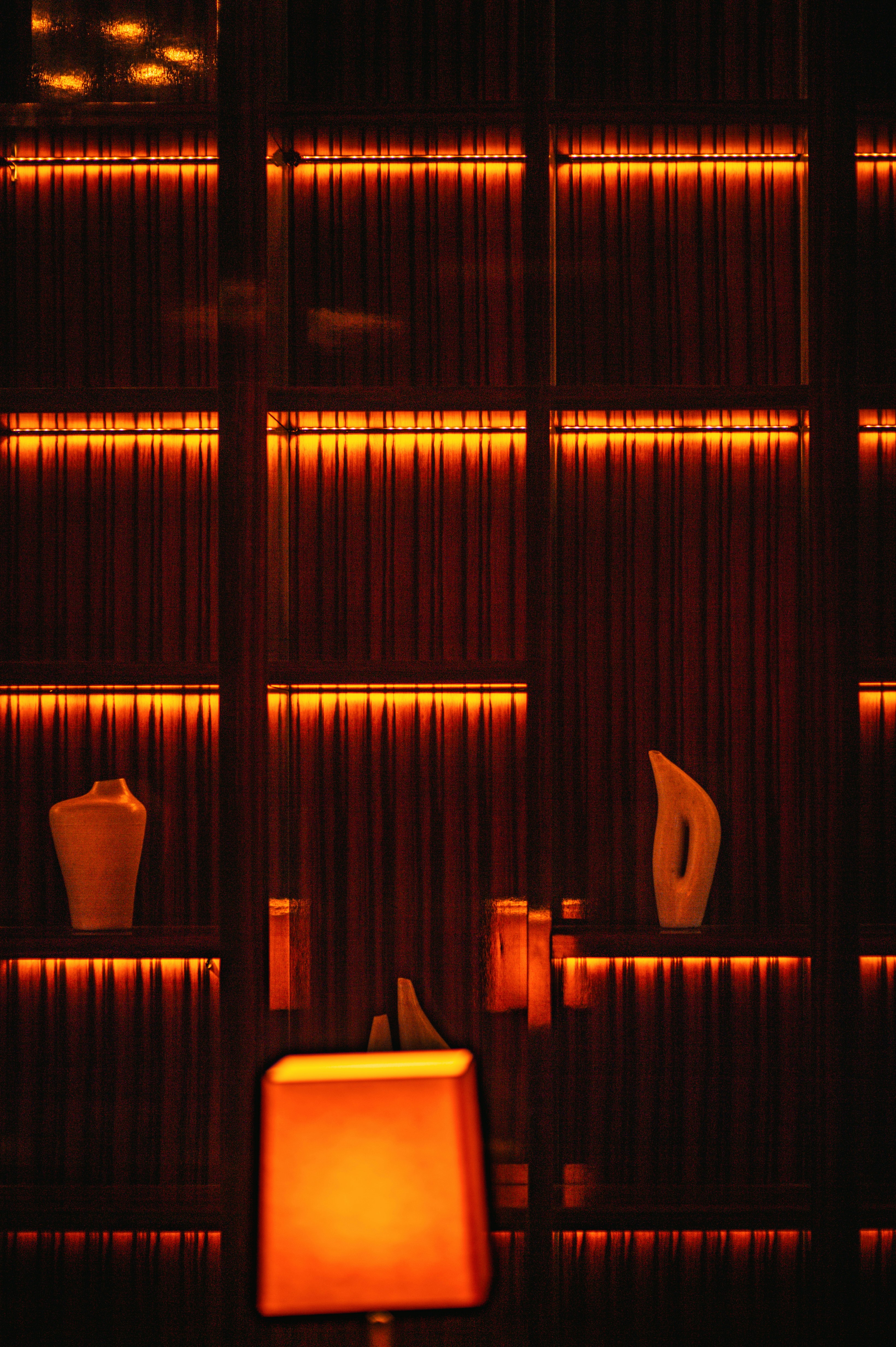 Des lumières orange chaudes illuminent les étagères avec des vases.