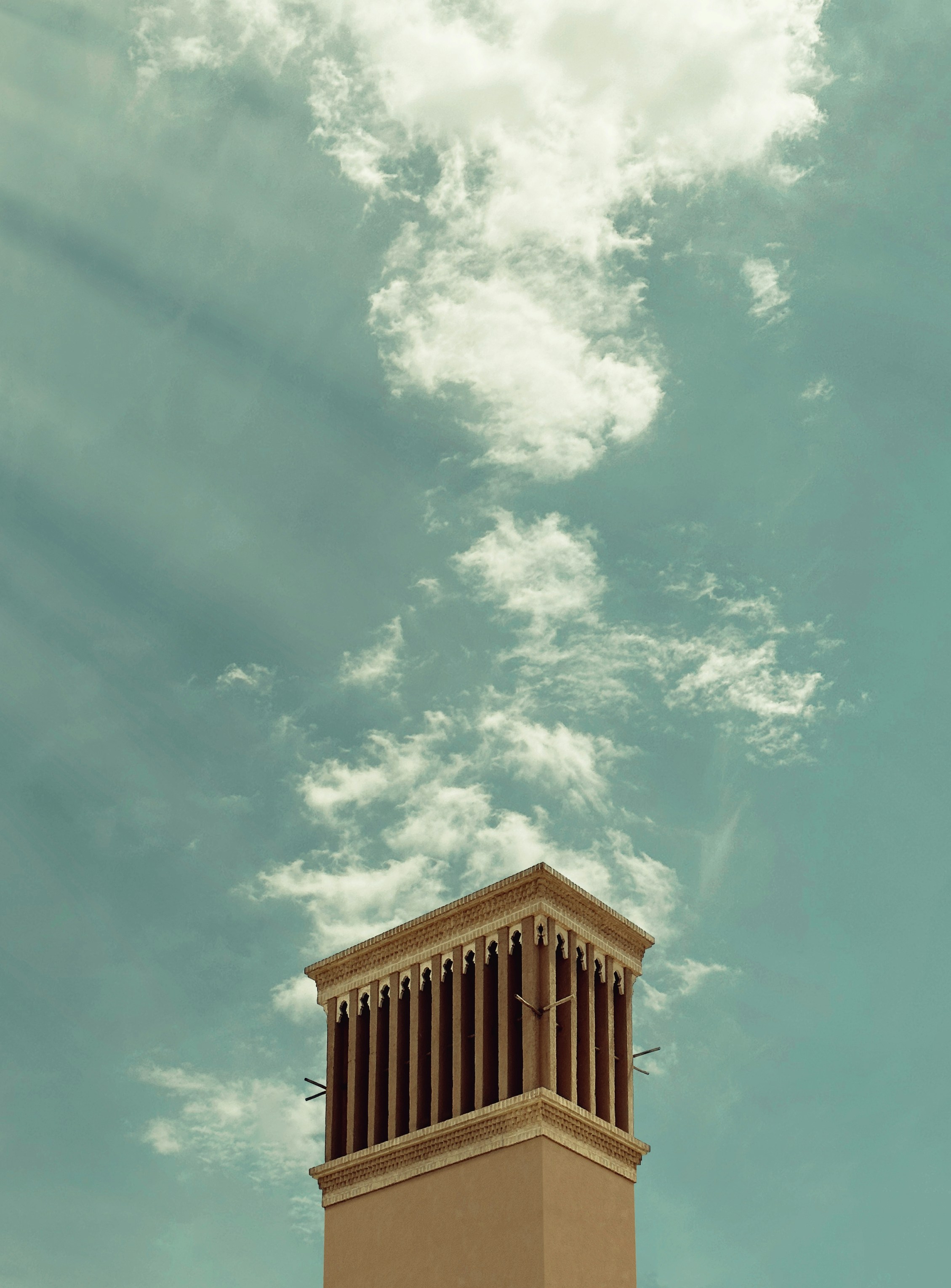 Une haute tour bronzée contre un ciel turquoise nuageux.