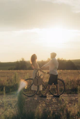 Couple with bicycle in field at sunset