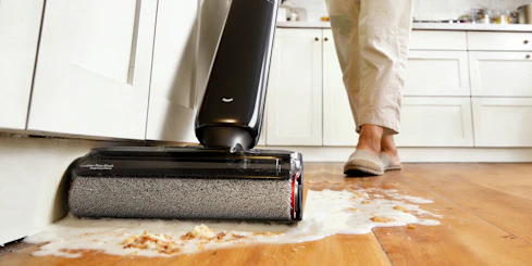 Person cleaning spilled liquid on wooden floor with vacuum