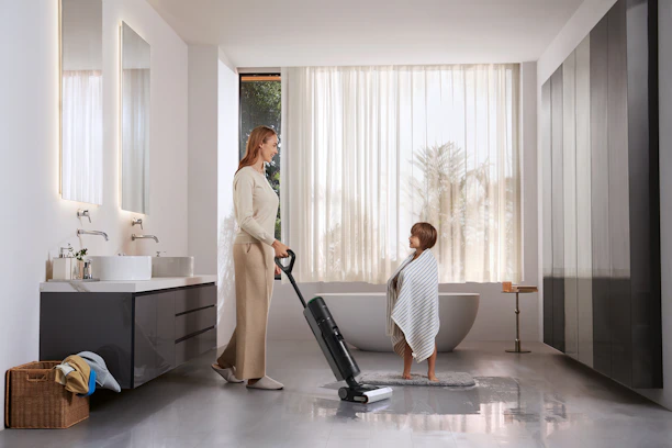 Woman vacuums bathroom while child watches