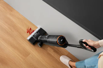 A person vacuuming spilled food on a wooden floor.