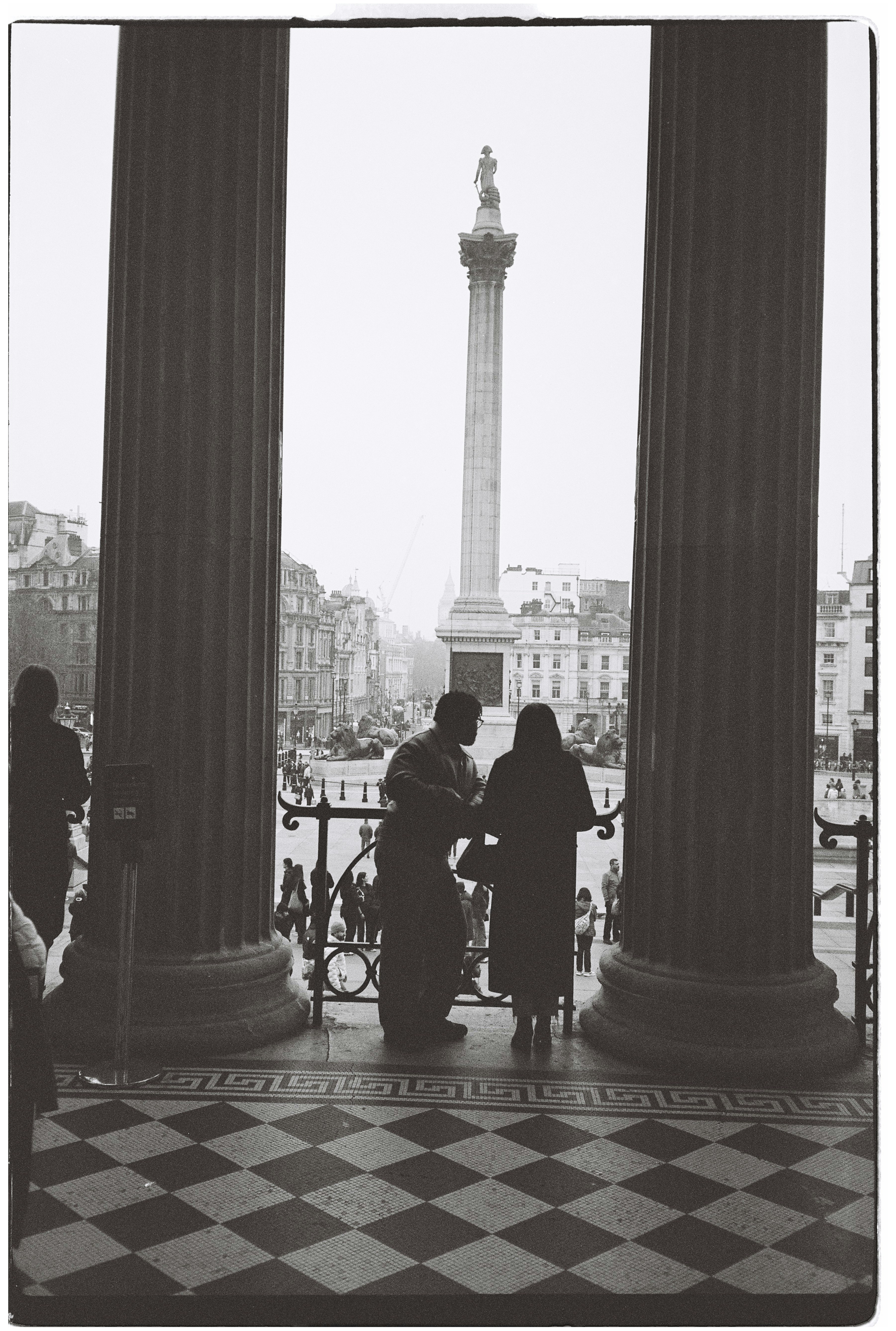 Two people stand looking at a monument in a square.