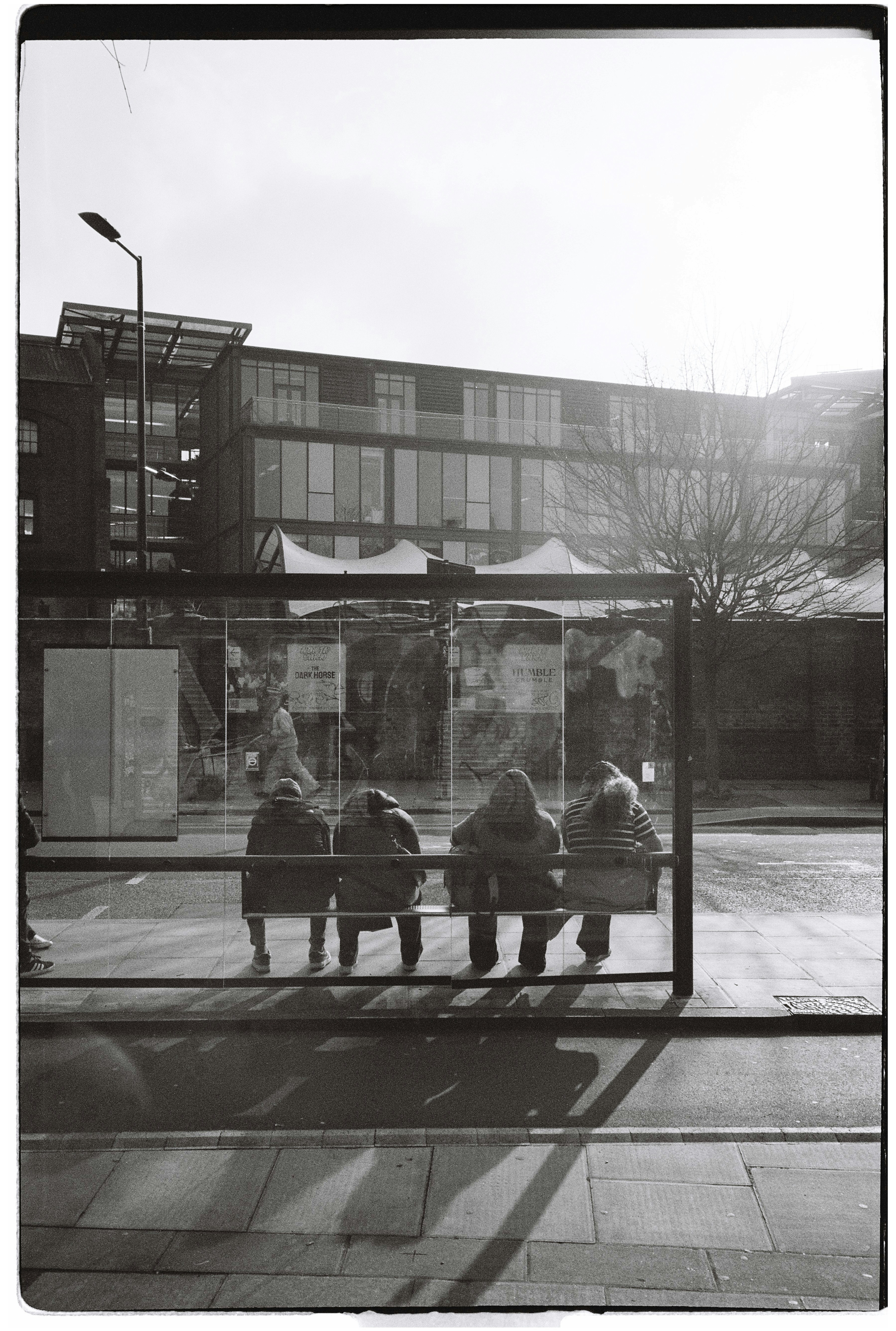 People sit at a bus stop on a sunny day.