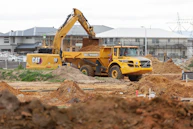 Yellow excavator loading dirt into dump truck at construction site.