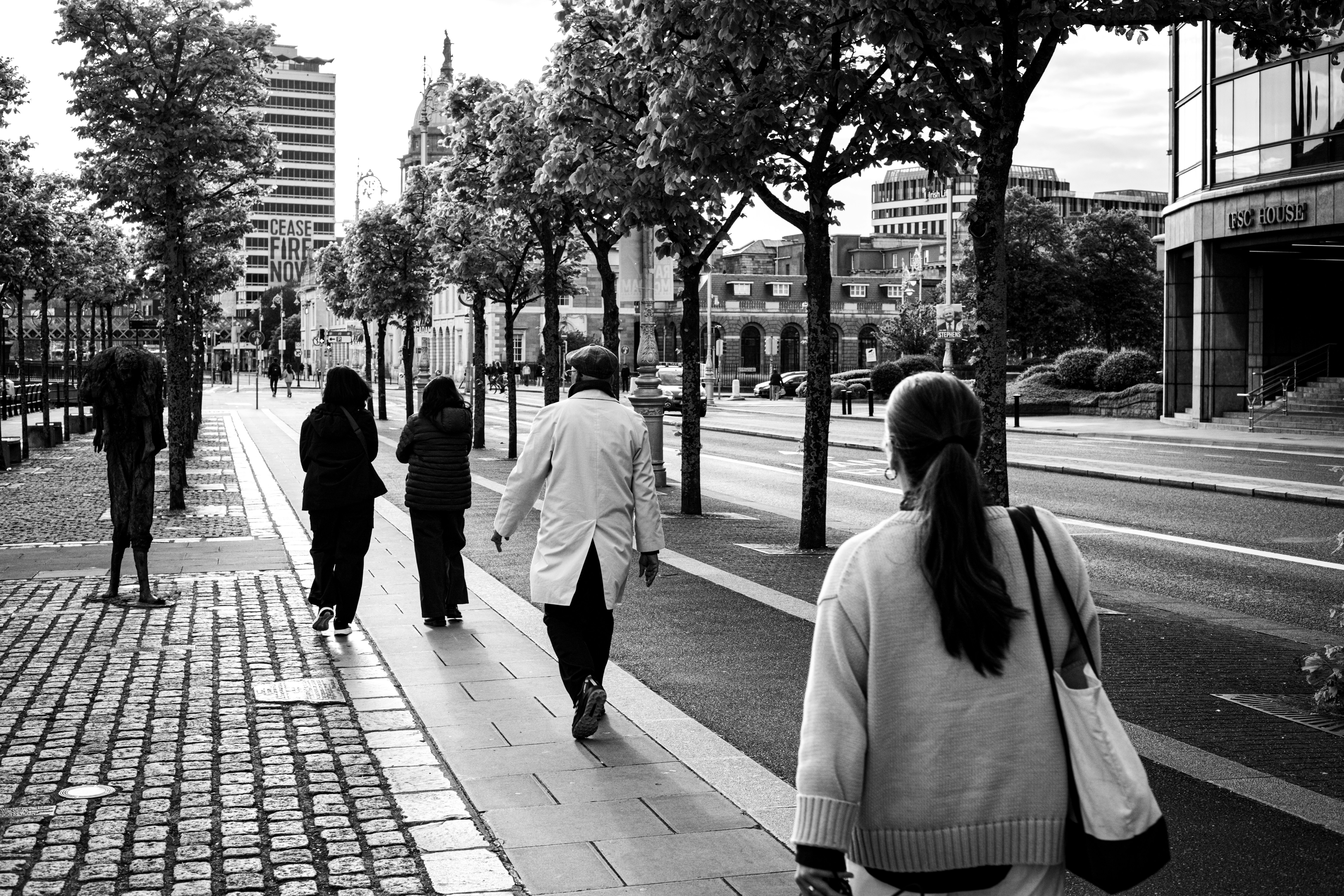 Gente caminando por una acera de ciudad bordeada de árboles.