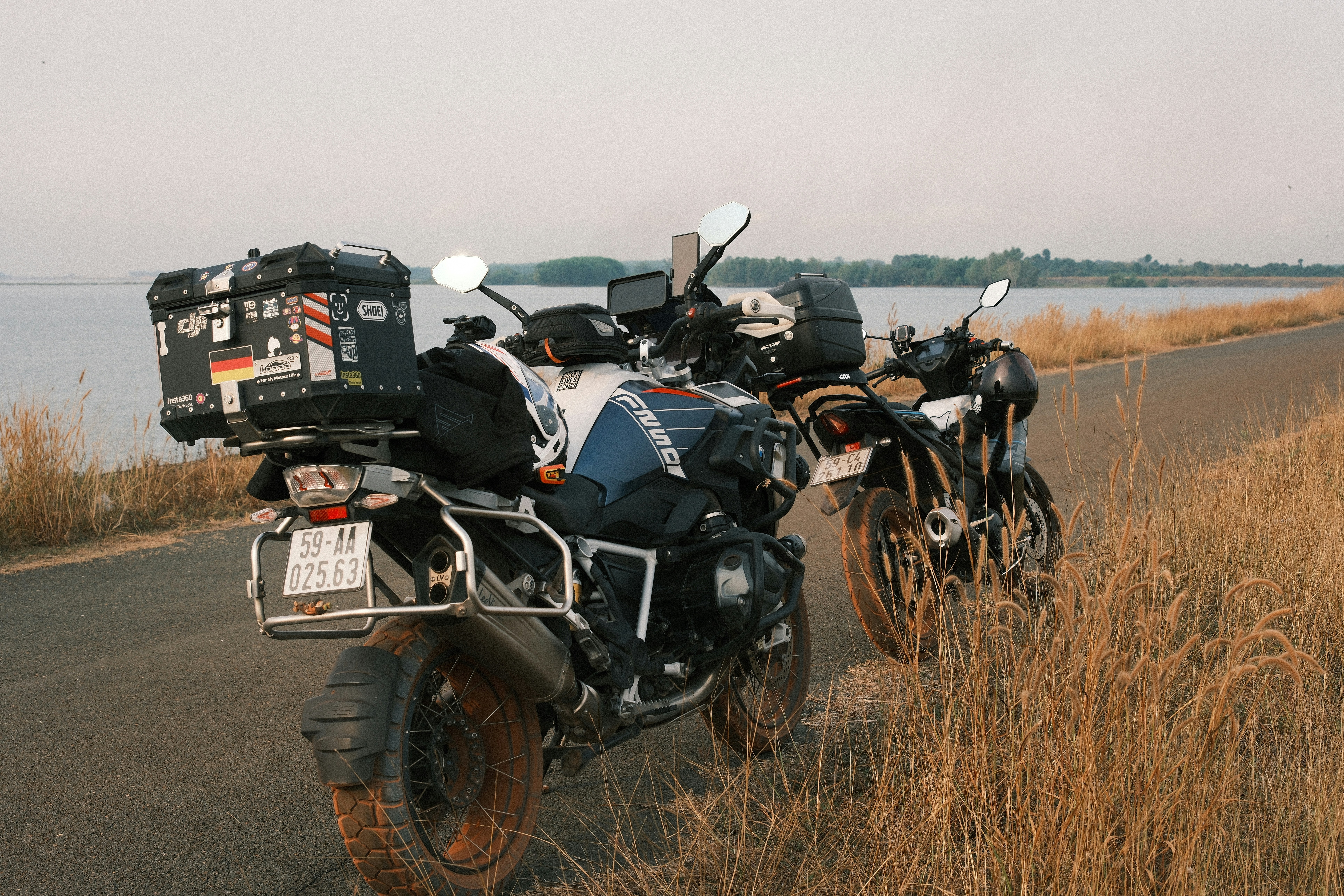 Two motorcycles parked on a road by a lake.
