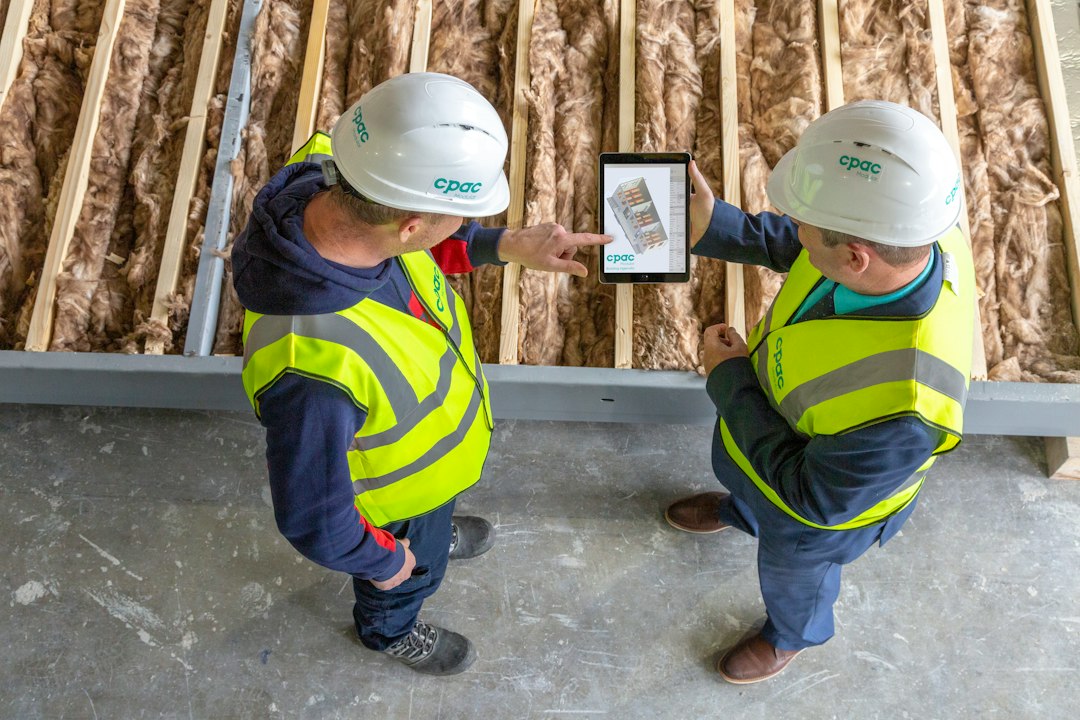 Two construction workers in hard hats reviewing job details on a tablet at a work site