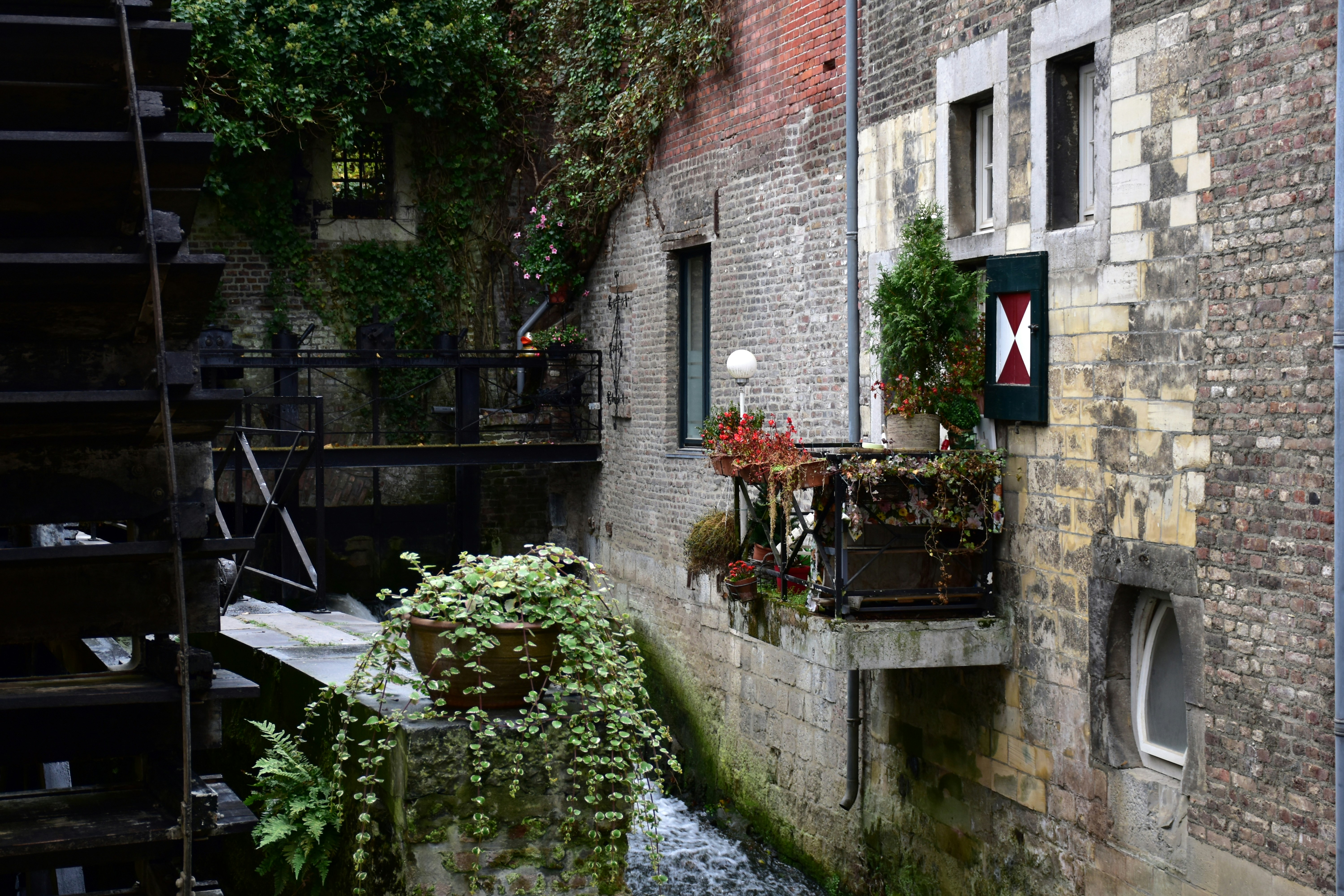 Old watermill with hanging plants and brick buildings.