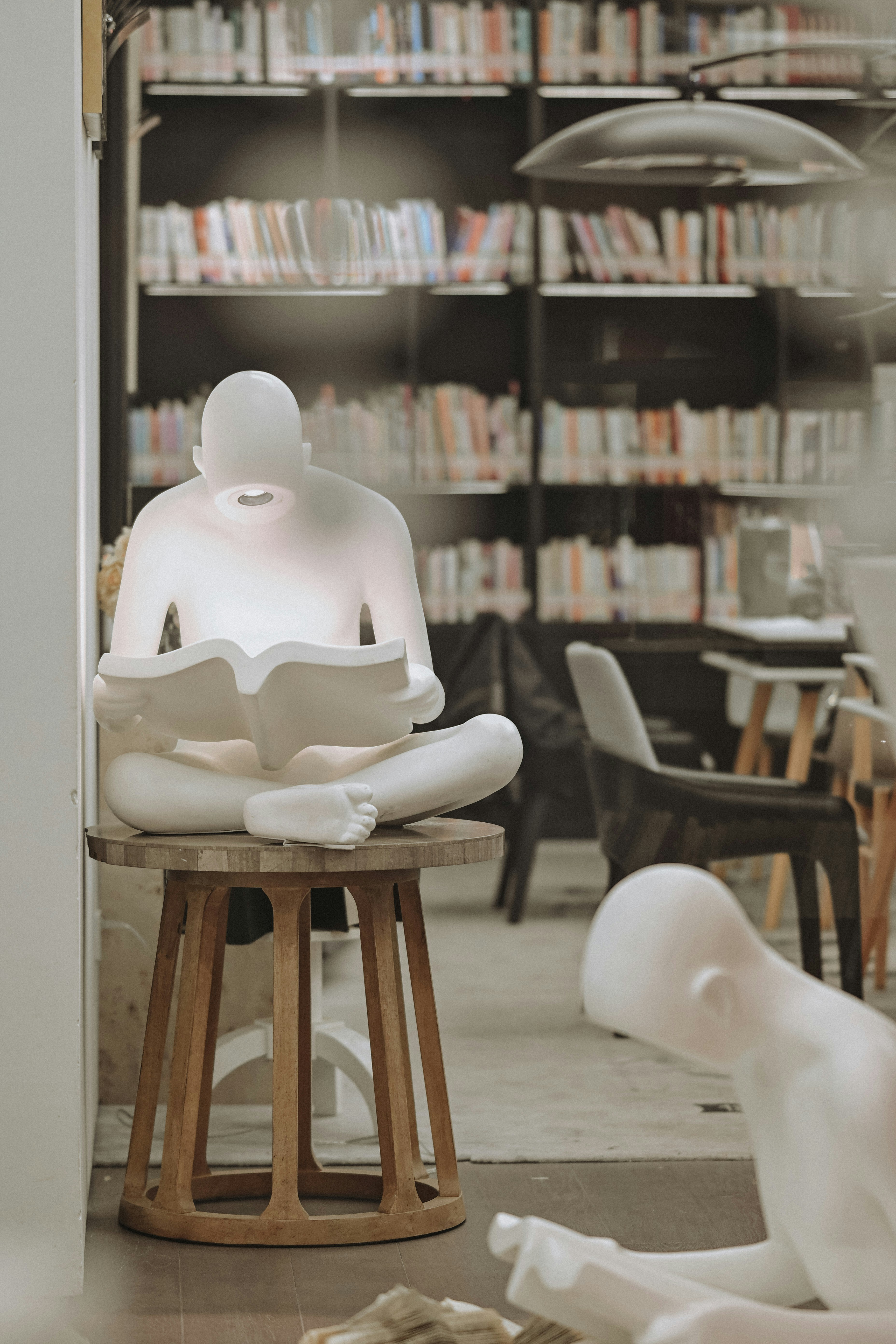 White sculpture of person reading a book in library.
