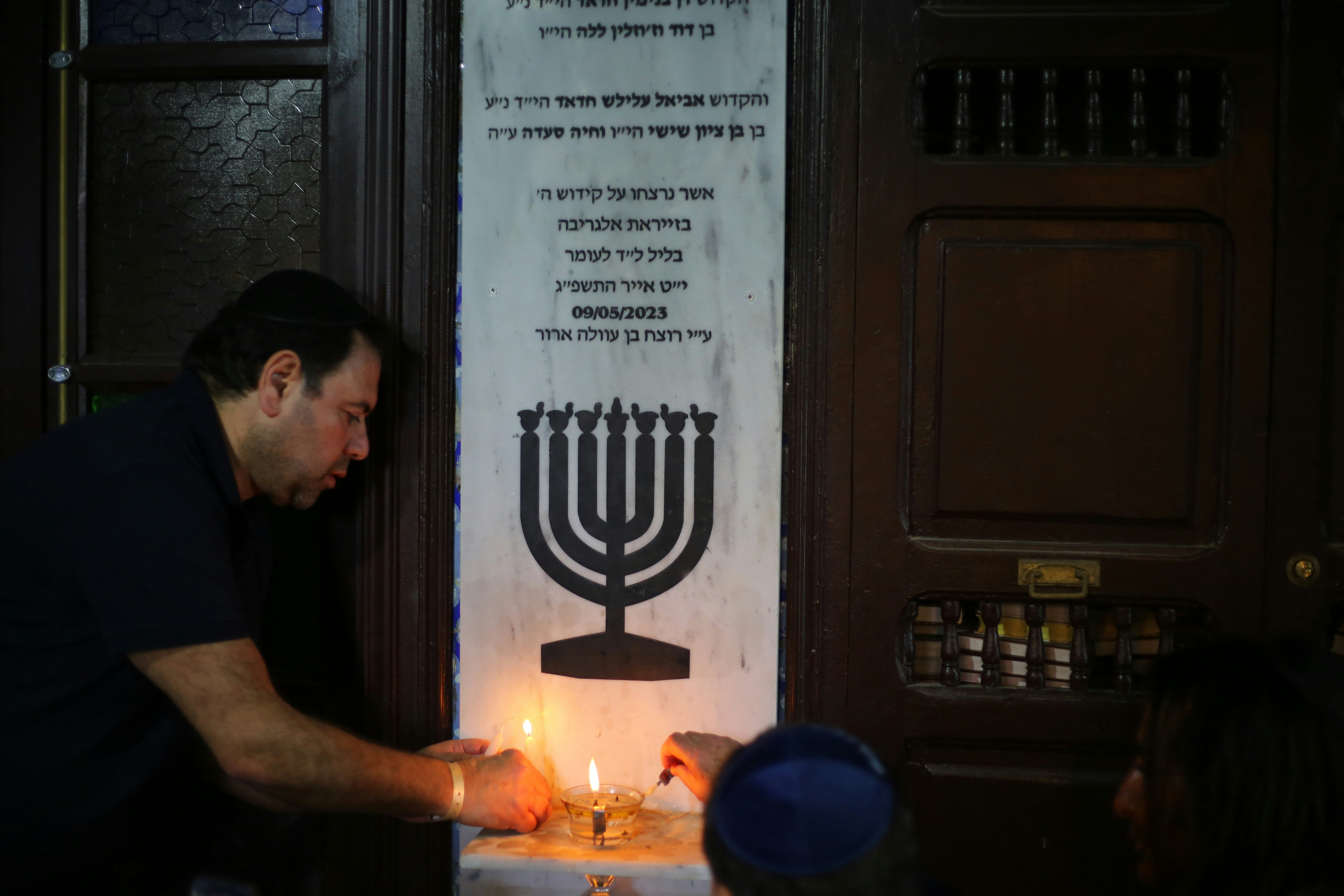 Man lights candles on a menorah with others watching people