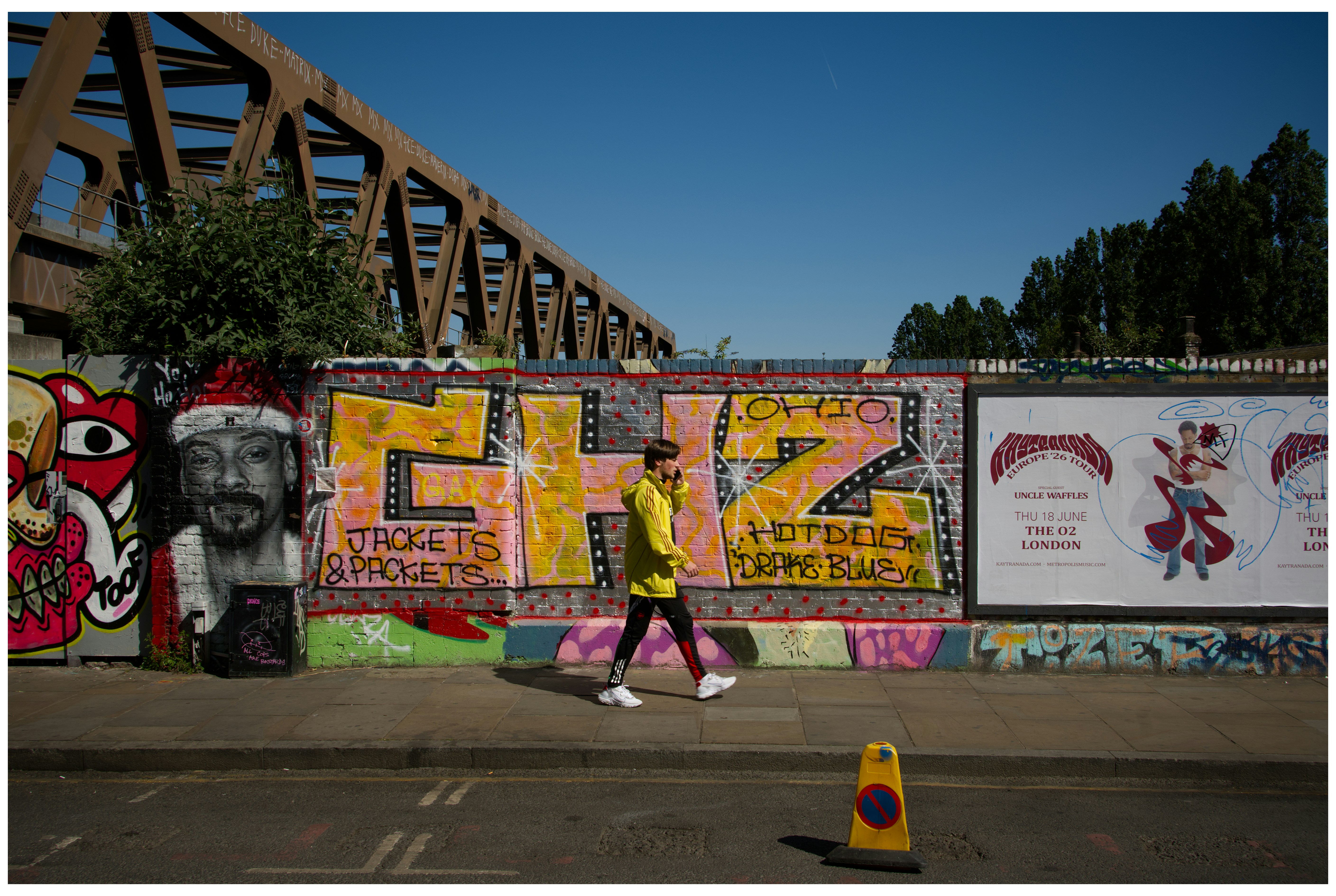 Person walks past graffiti-covered wall under bridge.
