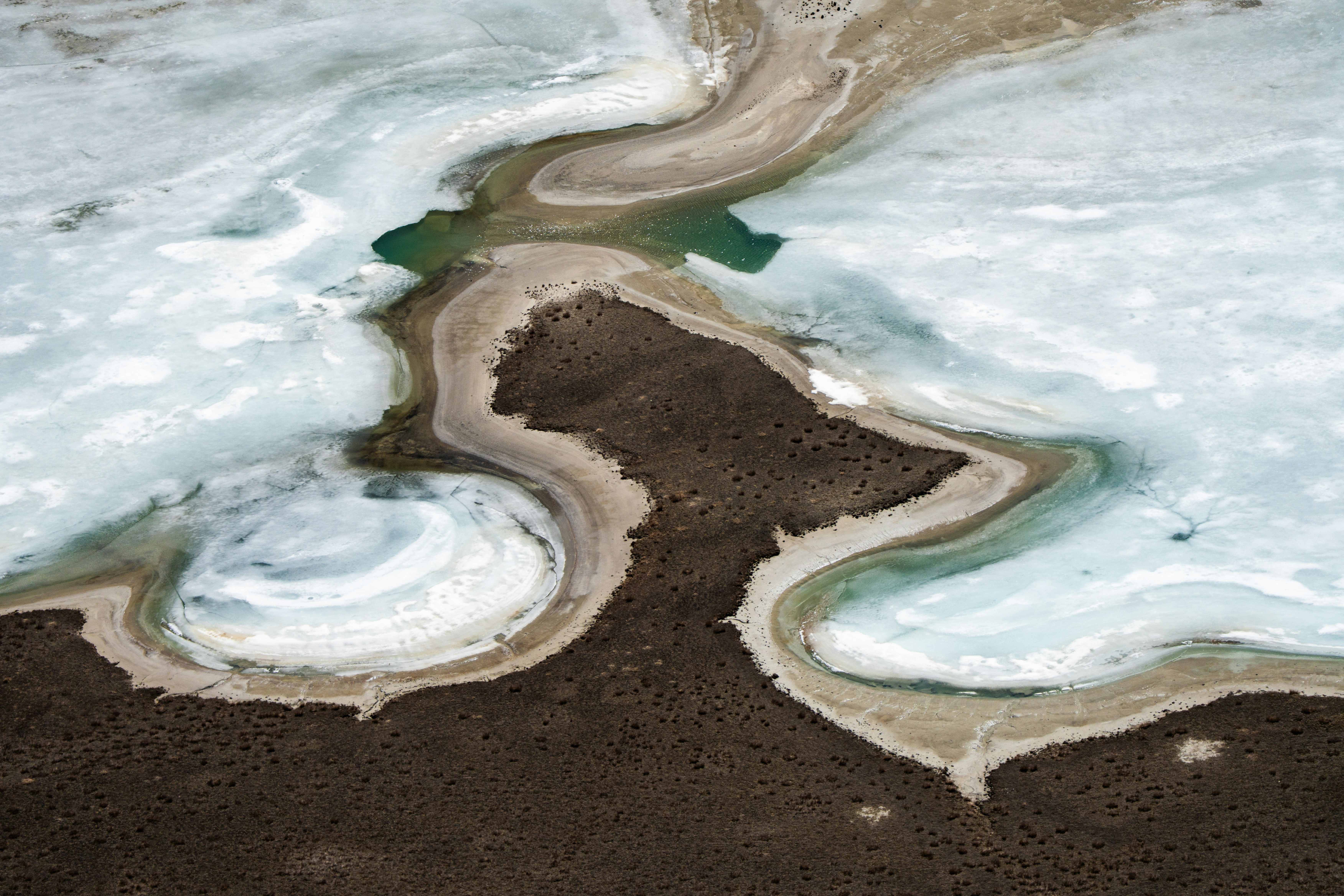 Aerial view of icy water and brown land formations.