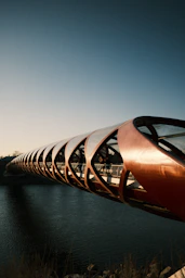 Modern curved bridge over dark water under clear sky