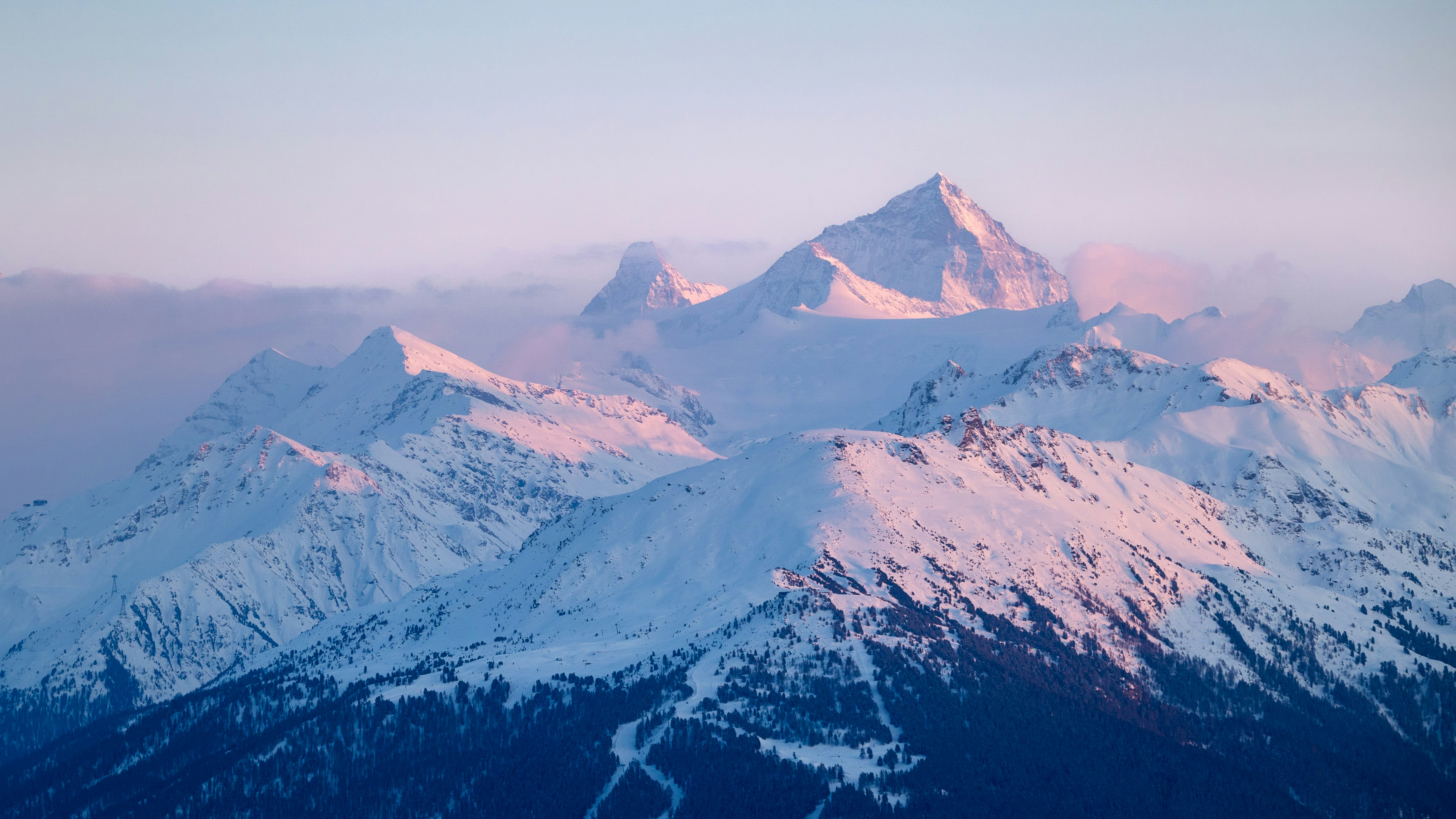 Snow-covered mountains bathed in soft pink sunrise light.