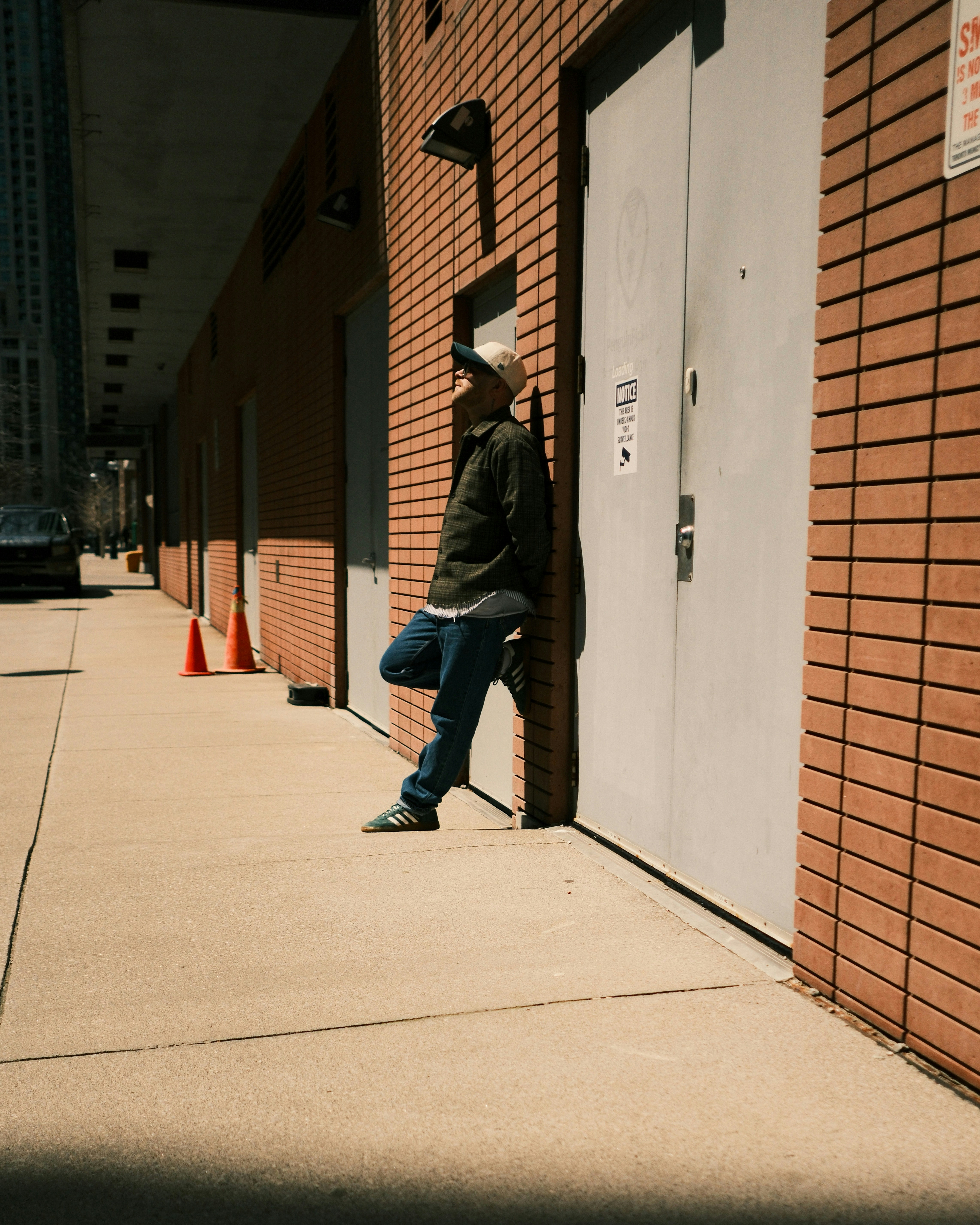 Man leaning against brick building on sidewalk.