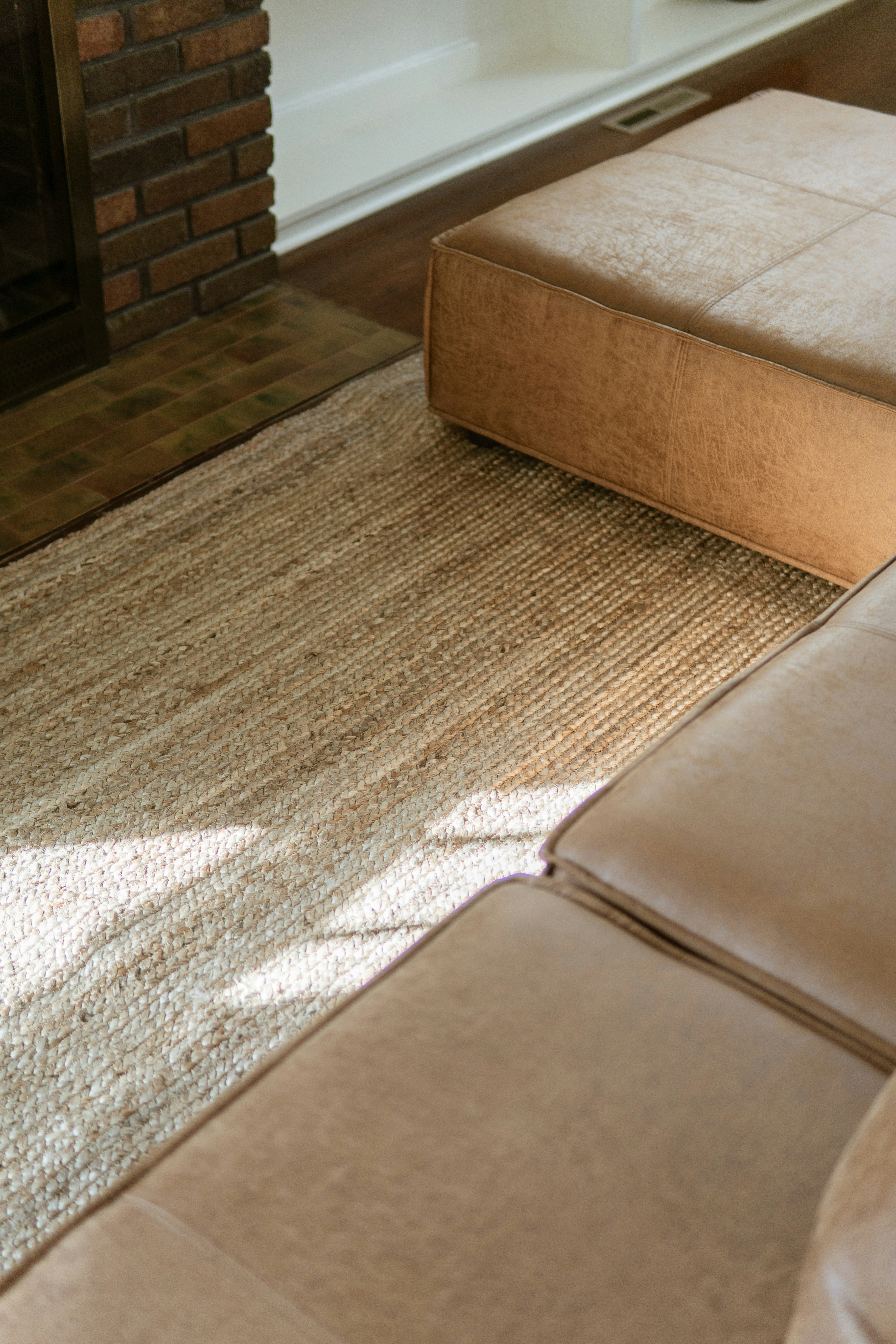 Sofa sectional kulit cokelat dan ottoman di atas karpet