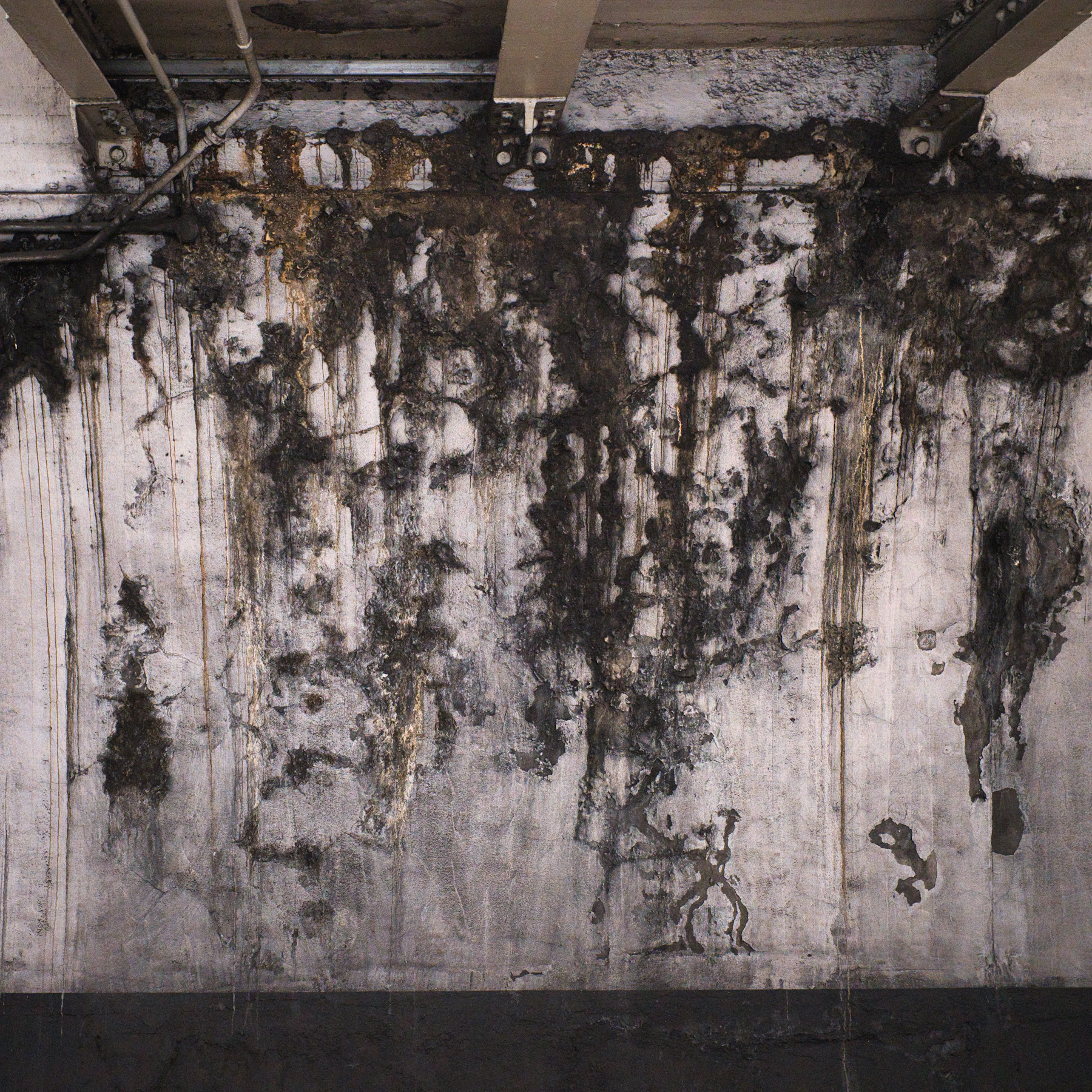 Water-damaged wall with dark staining and drip marks around building services