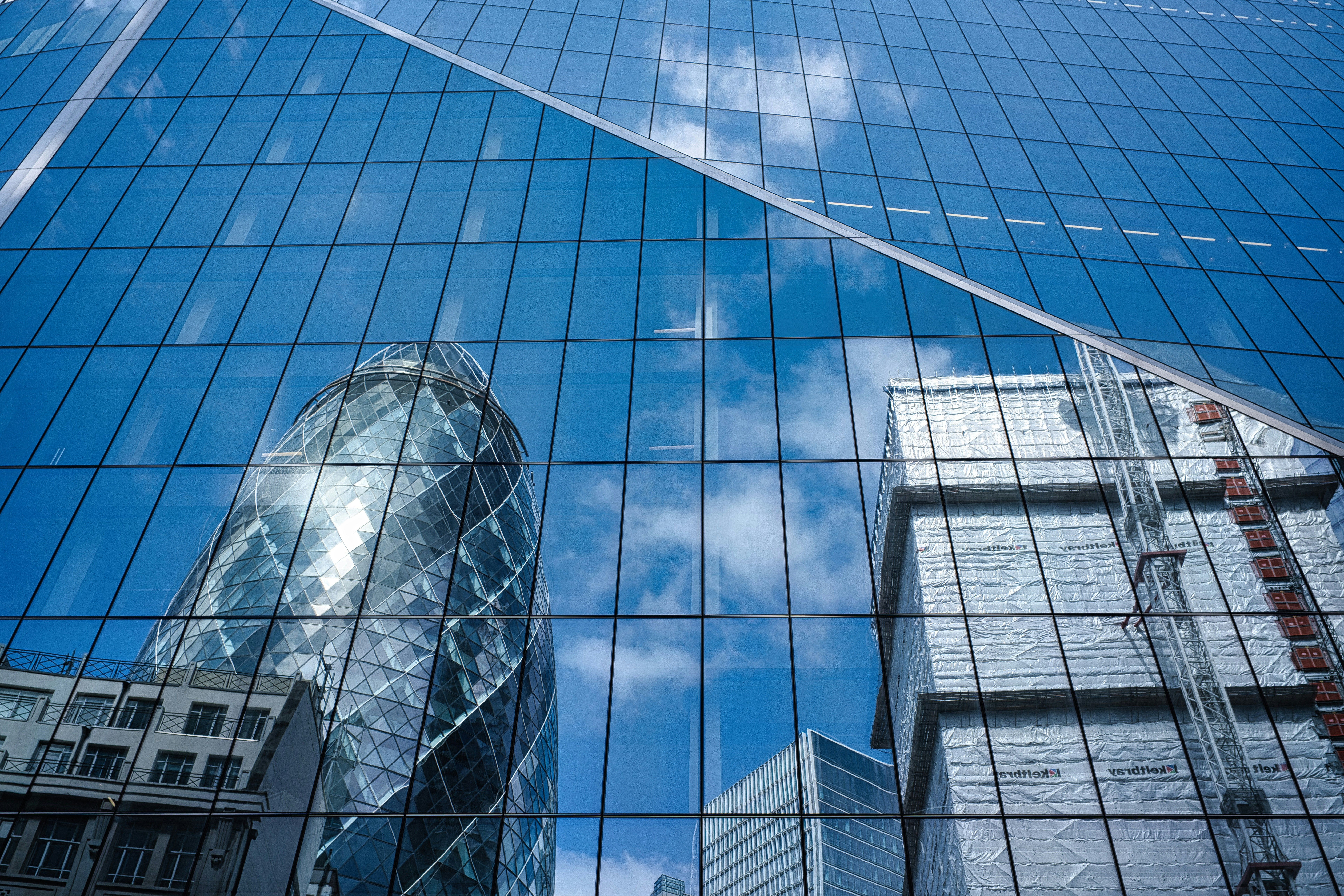 Prédios modernos de vidro refletindo céu azul e nuvens.