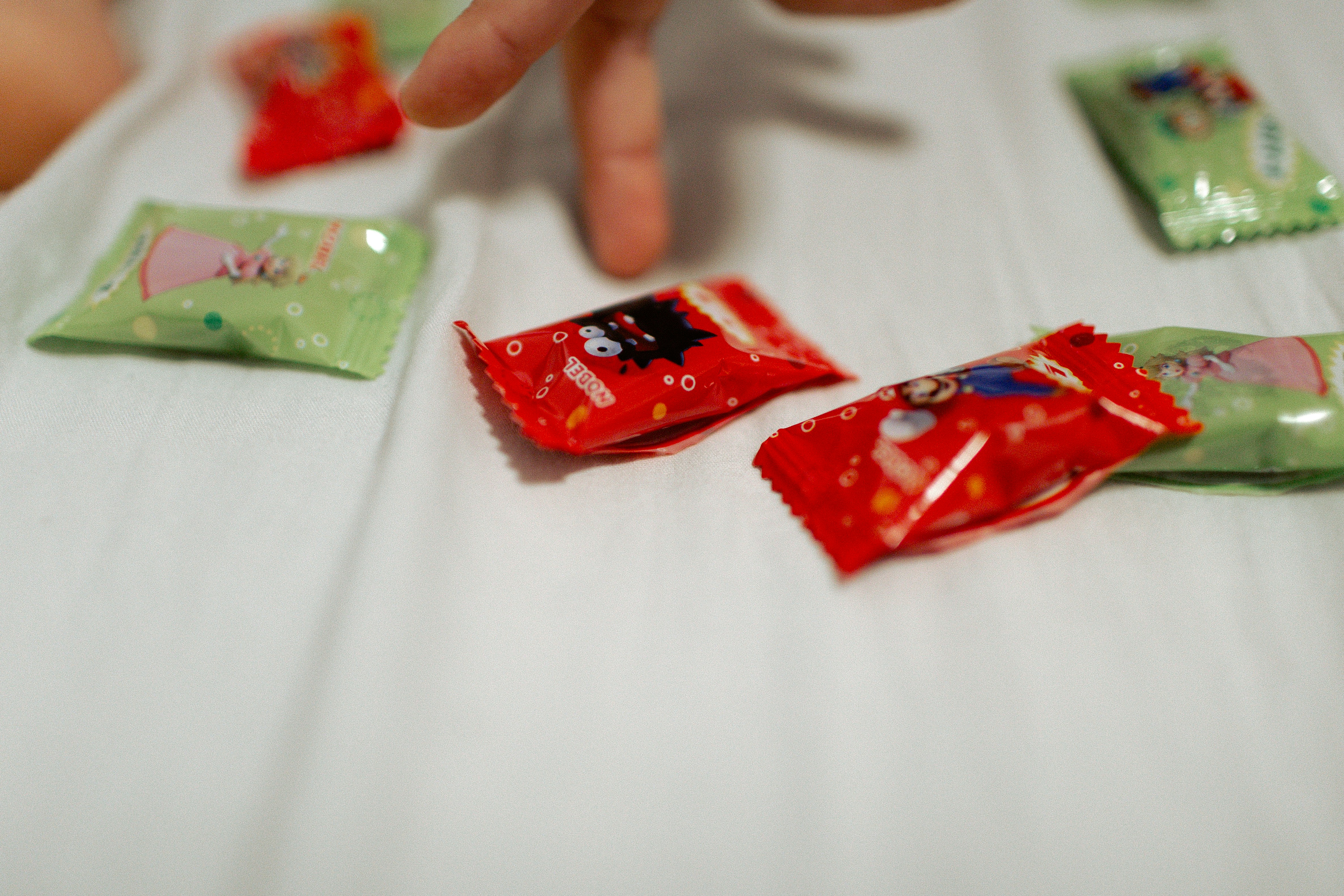 A hand reaches for wrapped candies on a white surface.